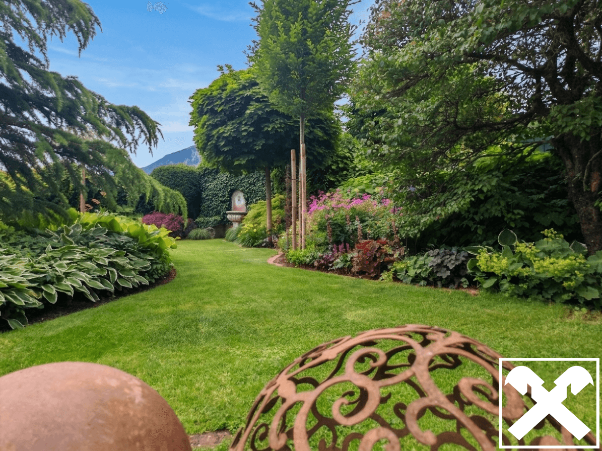 Gepflegter Garten mit Rasenflächen, Blumenbeeten und einem dekorativen Brunnen im Hintergrund.