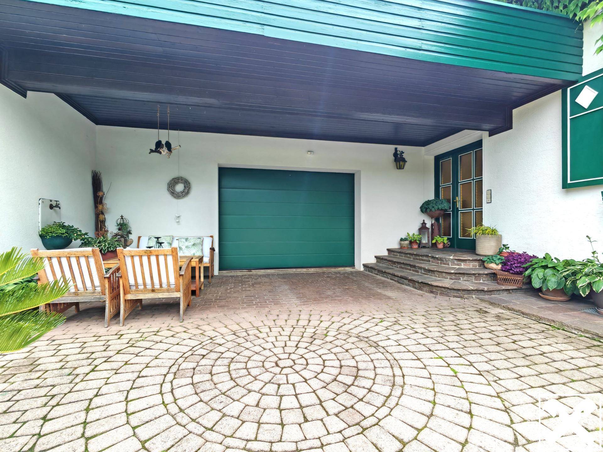 Überdachter Eingangsbereich mit Garage und einem kleinen Sitzbereich vor dem Haus.