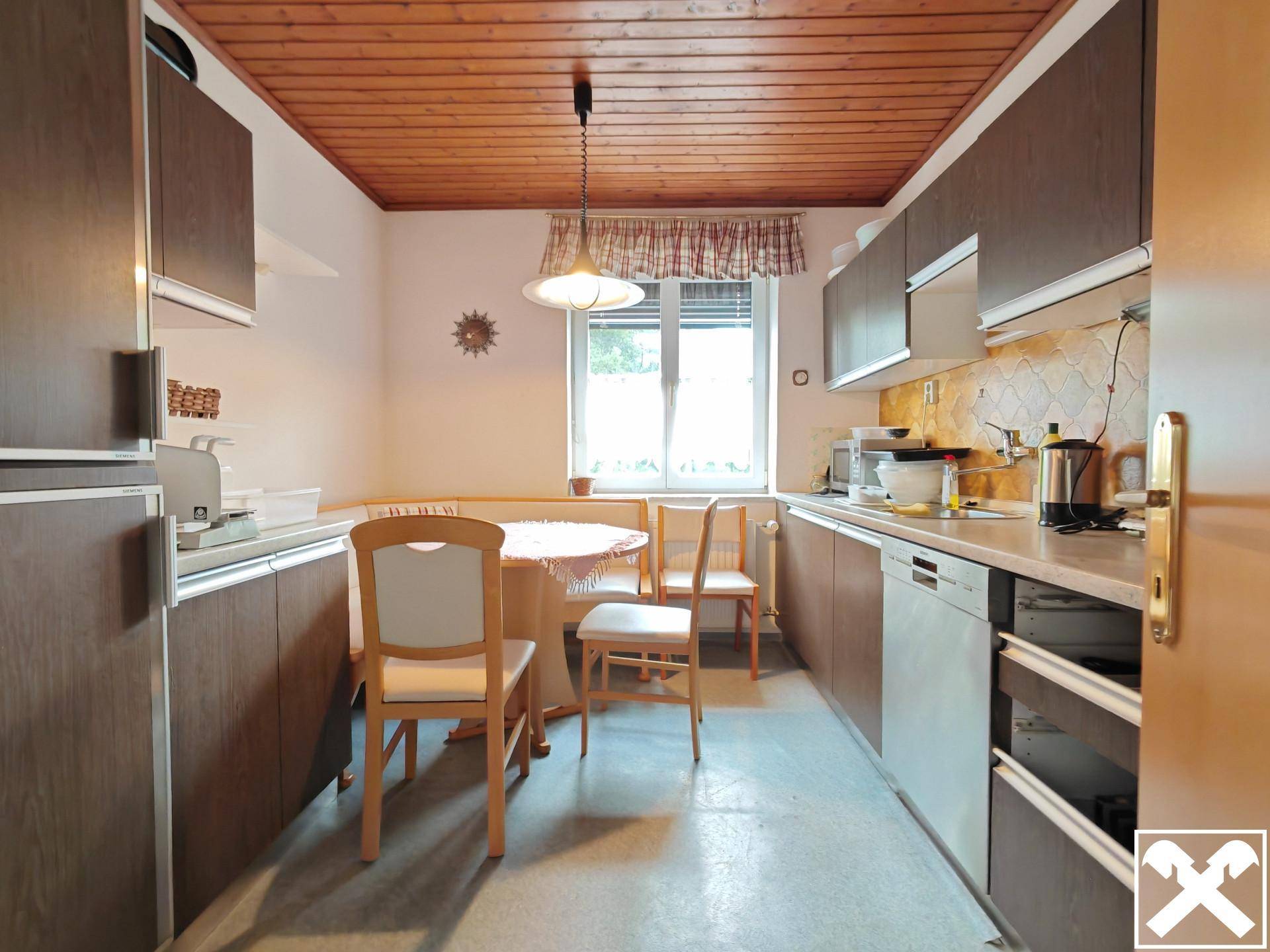 Funktionale Küche mit Holzdecke, Essbereich und braunen Einbauschränken.
