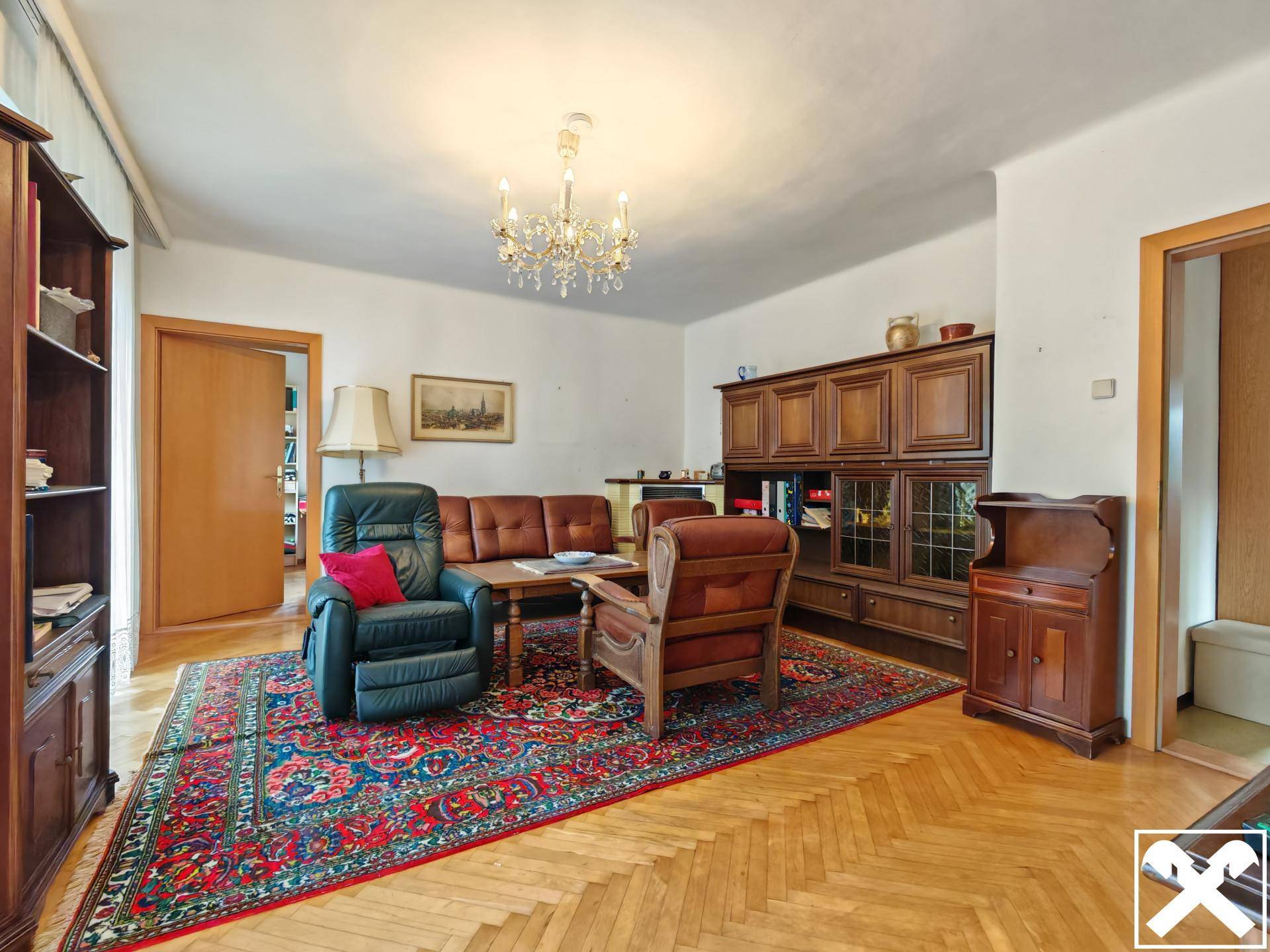 Klassisch eingerichtetes Wohnzimmer mit Parkettboden, großem Teppich und Holzmöbeln.