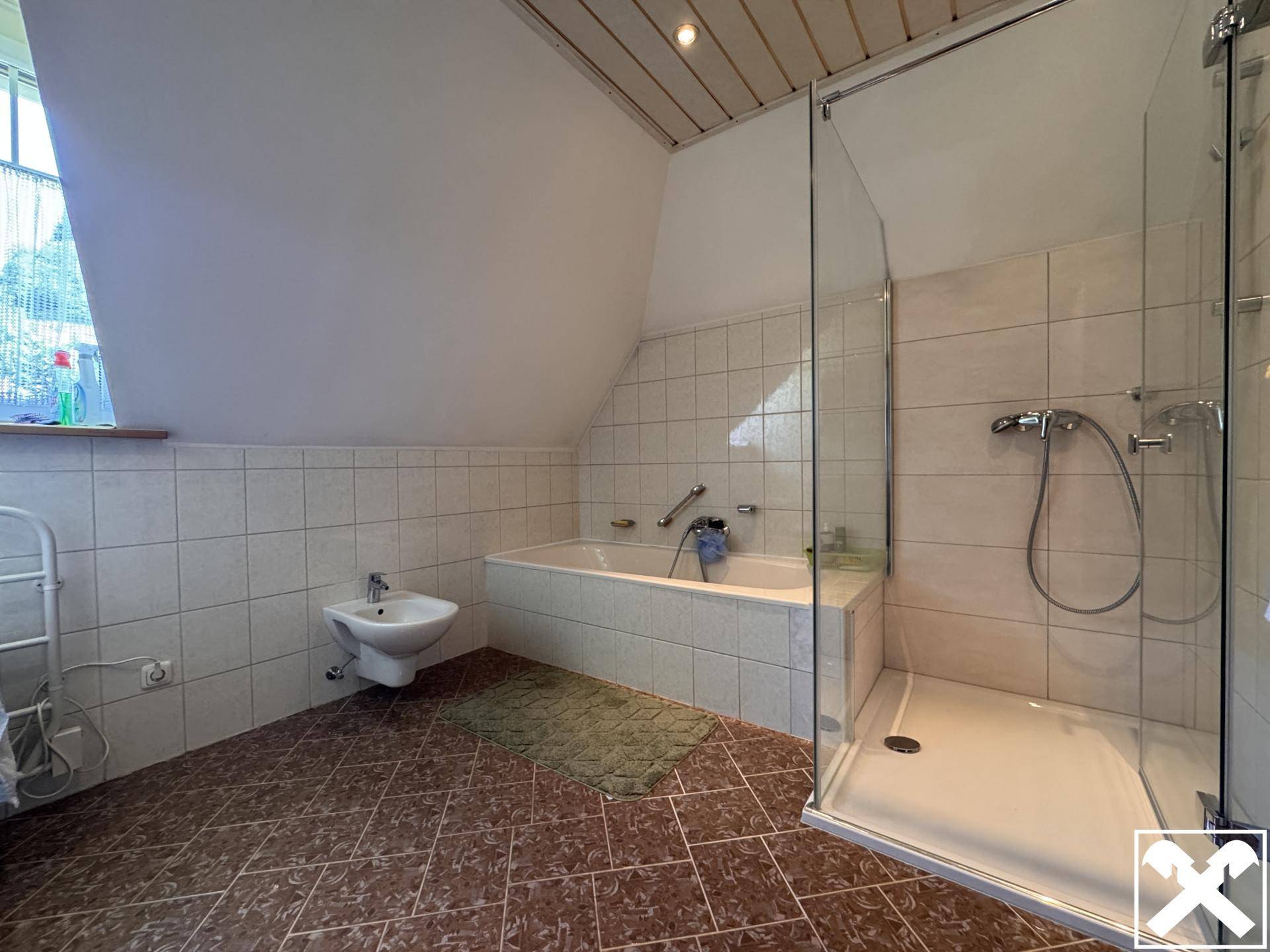 Badezimmer im Dachgeschoss mit Badewanne, Dusche, Bidet und schrägen Wänden.