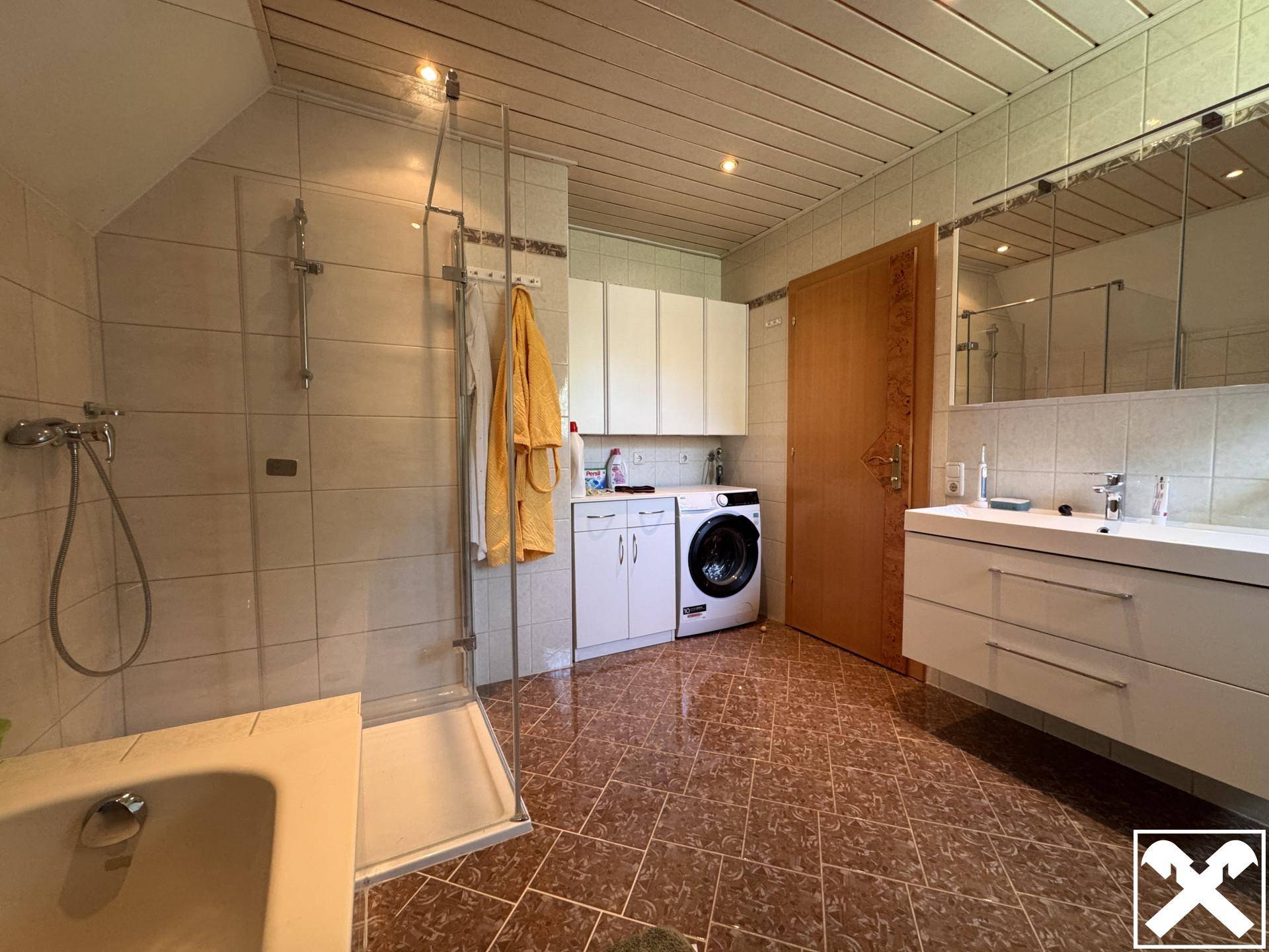 Helles Badezimmer mit Dusche, Doppelwaschbecken, Waschmaschine und Holzdecke.