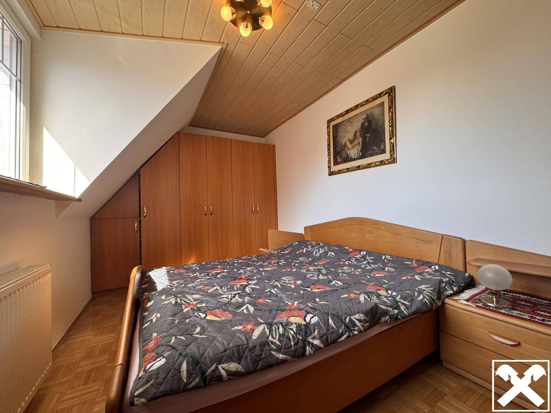 Schlafzimmer im Dachgeschoss mit Holzboden, Einbauschränken und schräger Decke.