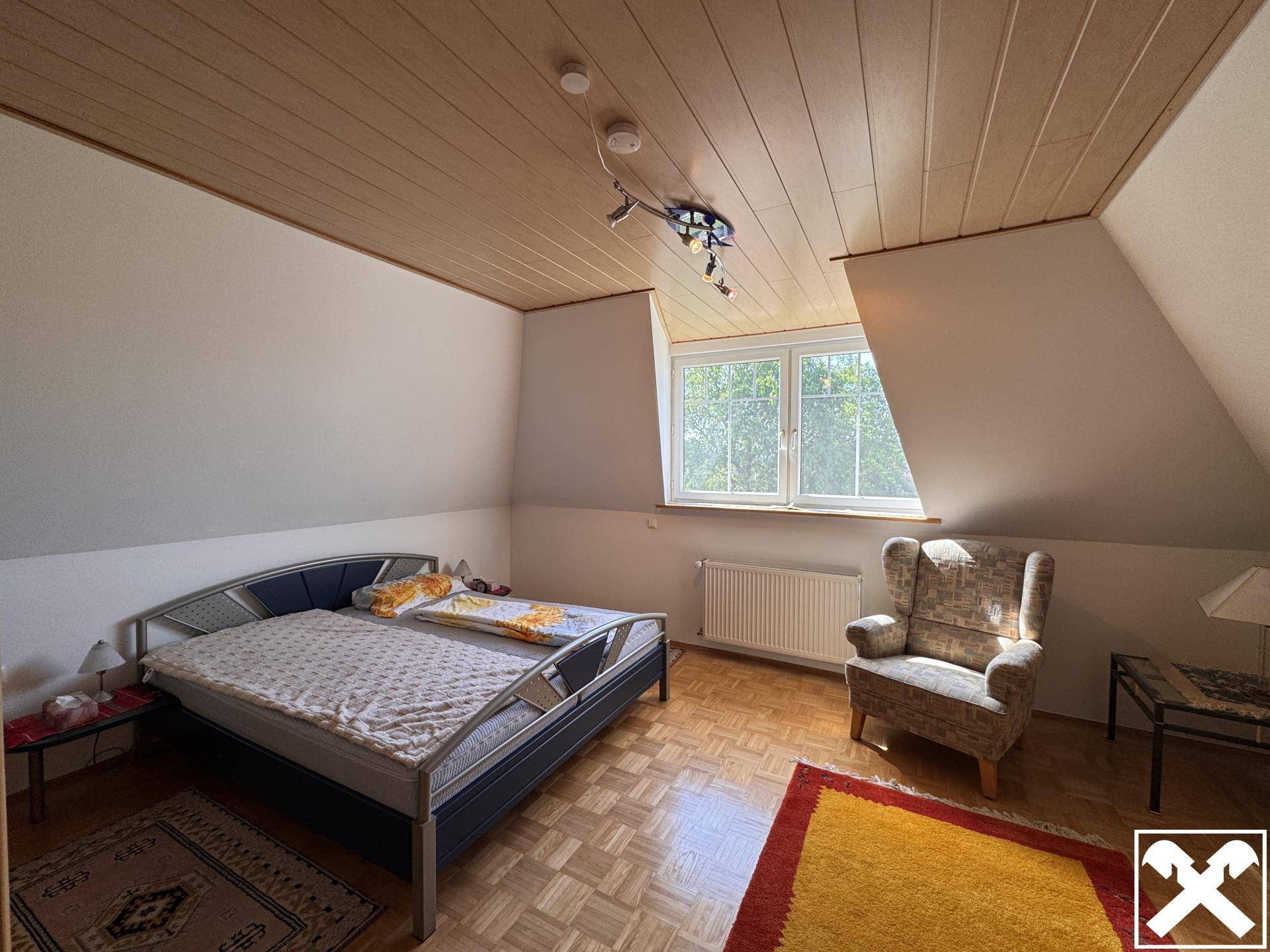 Geräumiges Schlafzimmer im Dachgeschoss mit Holzboden, großem Bett und gemütlichem Sessel.