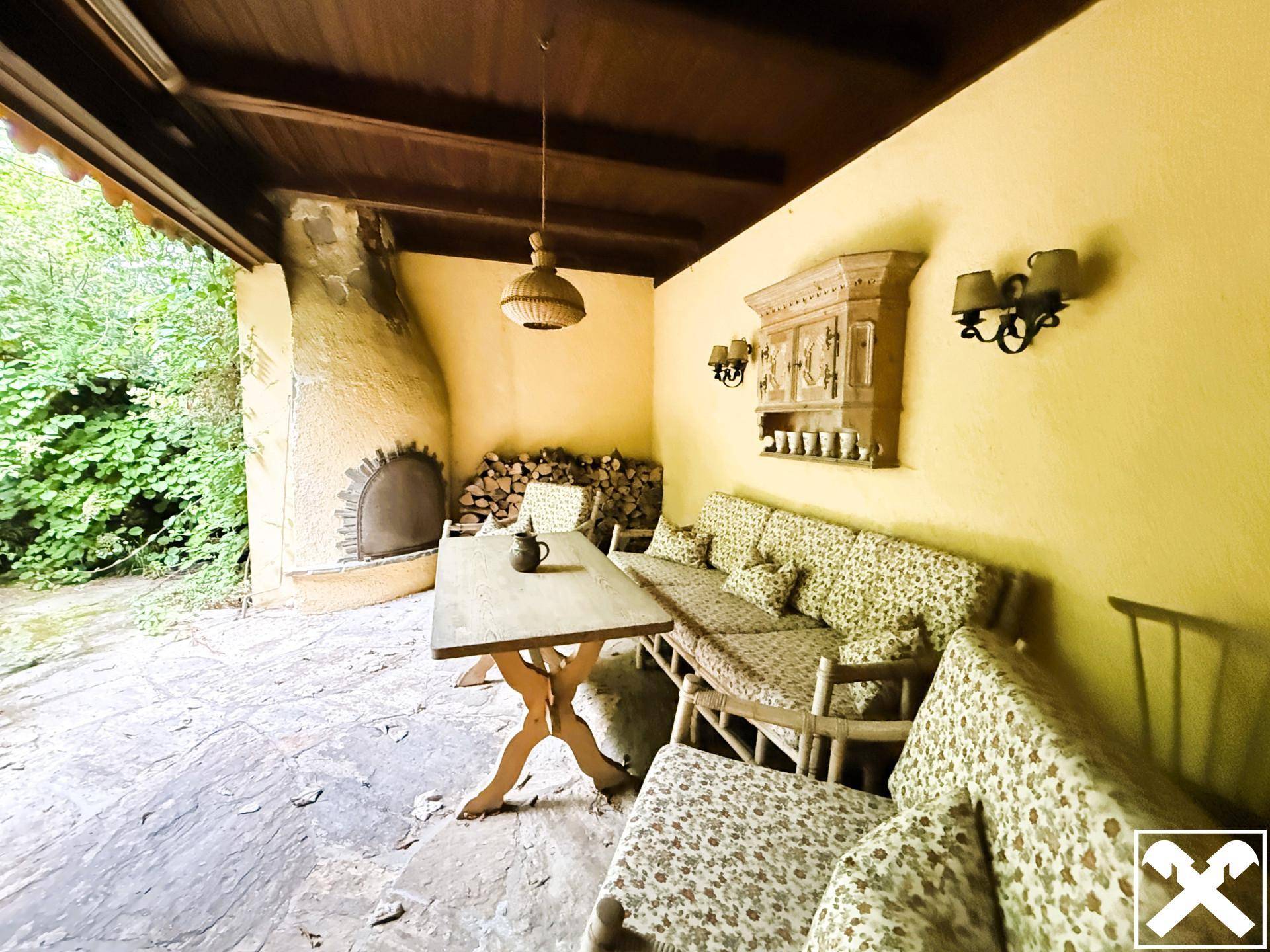 Gemütliche überdachte Terrasse mit Außenkamin und rustikalen Sitzgelegenheiten im Grünen.