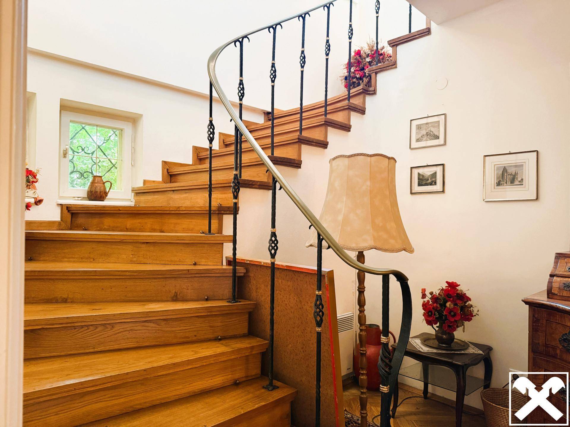 Elegantes Holztreppenhaus mit schmiedeeisernem Geländer und dekorativer Beleuchtung.