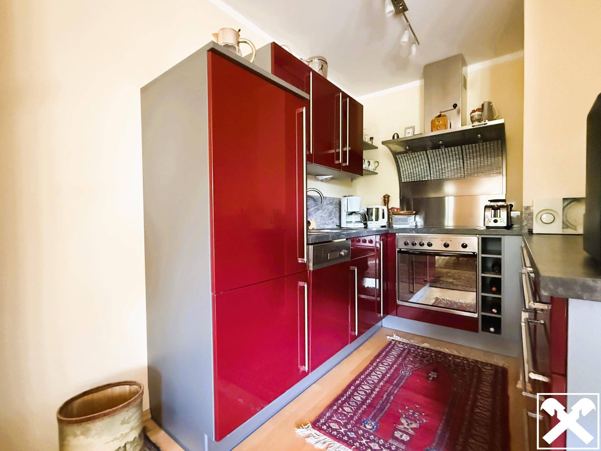 Moderne Küche mit glänzenden roten Schränken, integrierten Geräten und einem Teppich auf dem Holzboden.