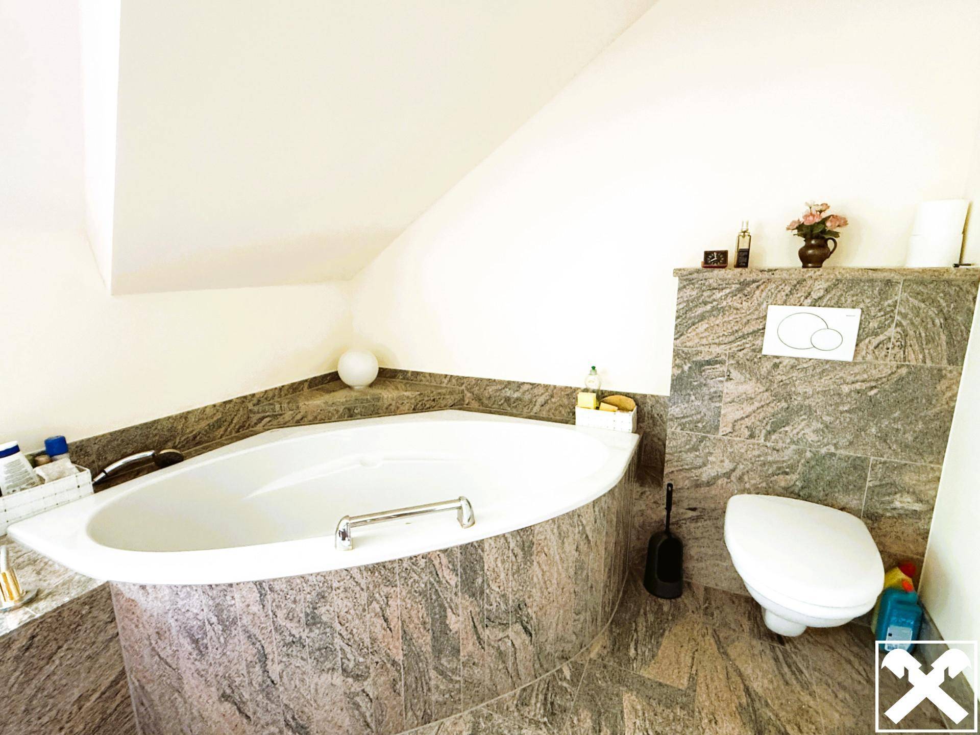 Badezimmer mit Eckbadewanne und Toilette, ausgestattet mit Granitfliesen und einer Dachschräge.
