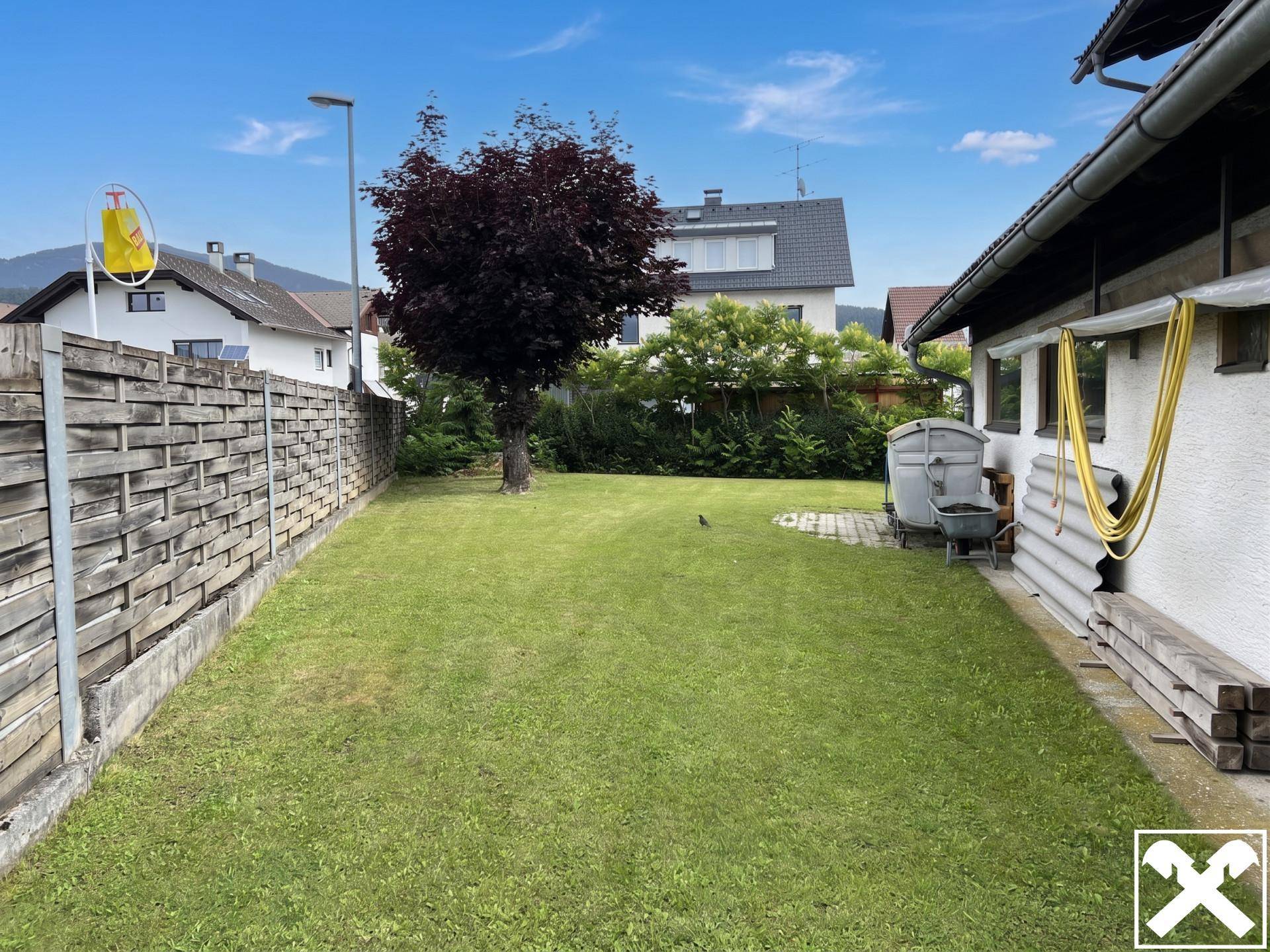 Hinterhof mit Rasenfläche, Holzzaun und einem Baum, umgeben von Wohnbebauung.