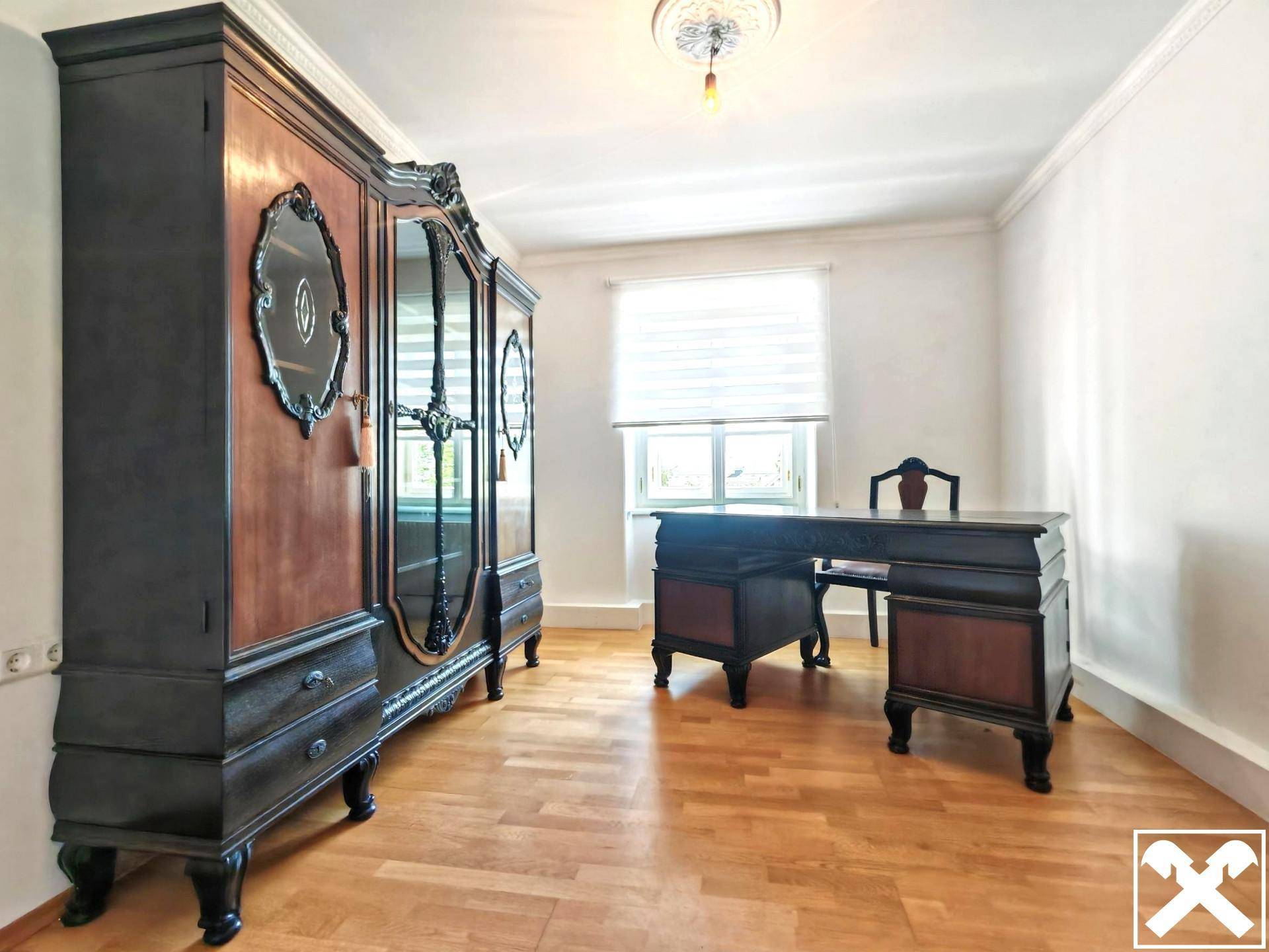 Arbeitszimmer mit antikem Schreibtisch, großem Holzschrank und hellem Parkettboden.
