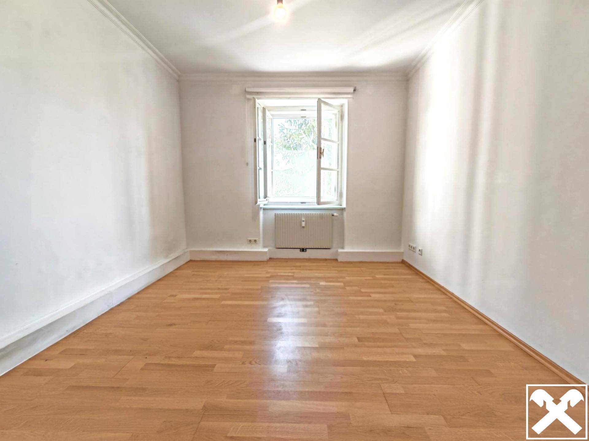 Leerer Raum mit hellem Parkettboden, weißen Wänden und einem geöffneten Fenster für frische Luft.