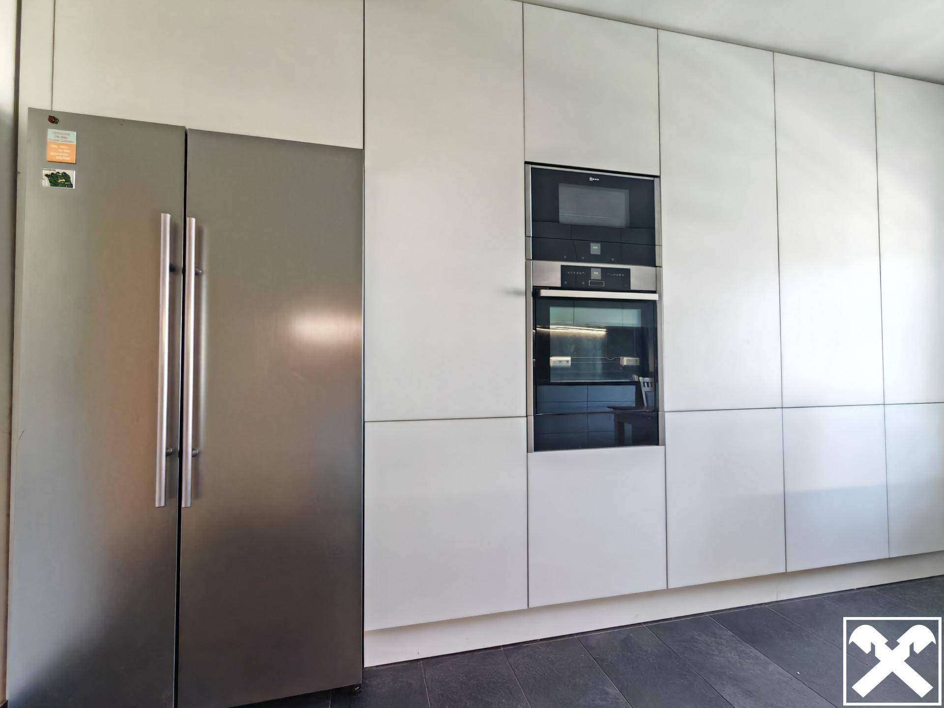 Moderne Küchenzeile mit integrierten Geräten wie Backofen, Mikrowelle und großem Kühlschrank.