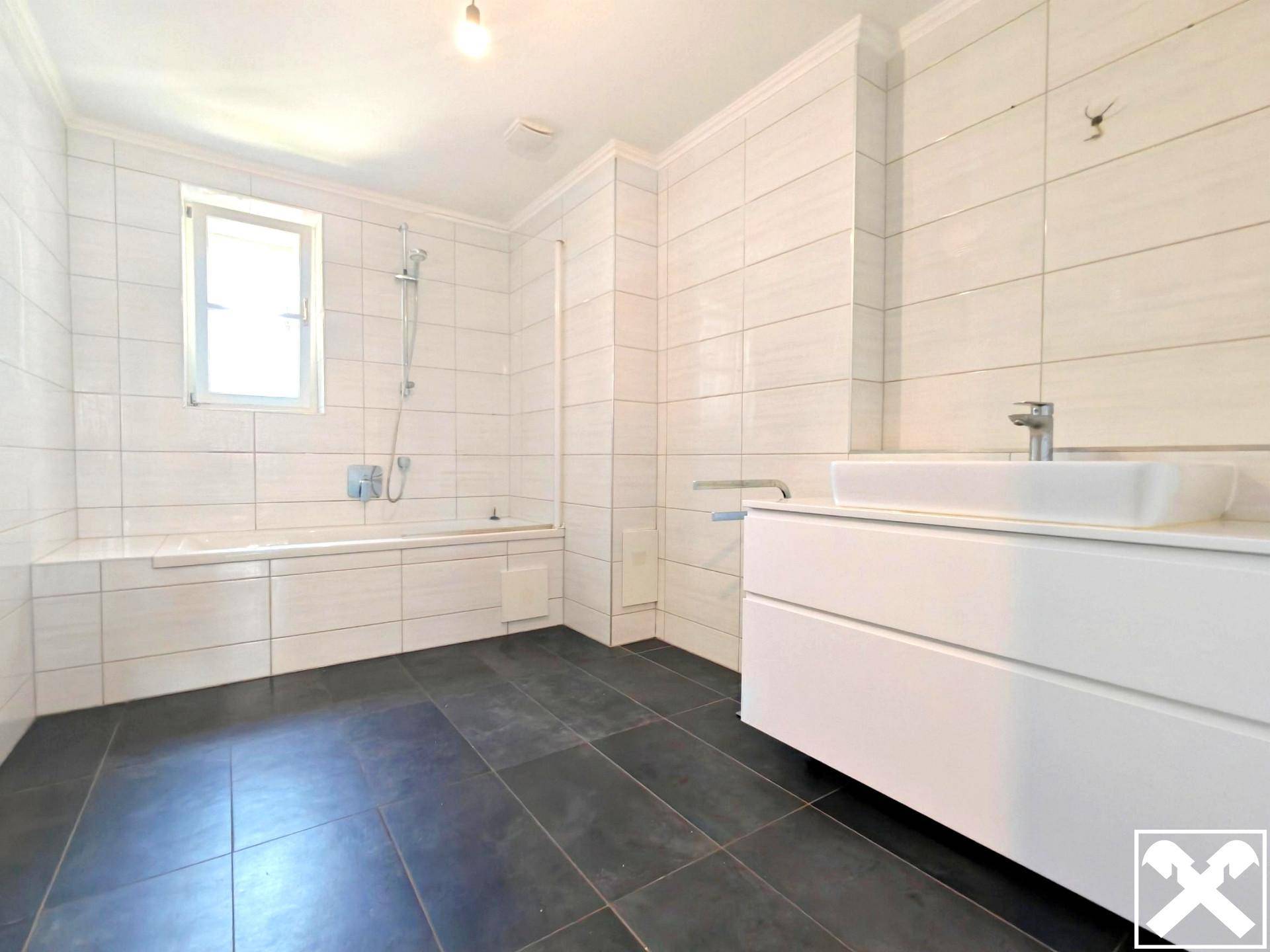 Modernes Badezimmer mit Badewanne, schwebendem Waschtisch und weißen Wandfliesen.