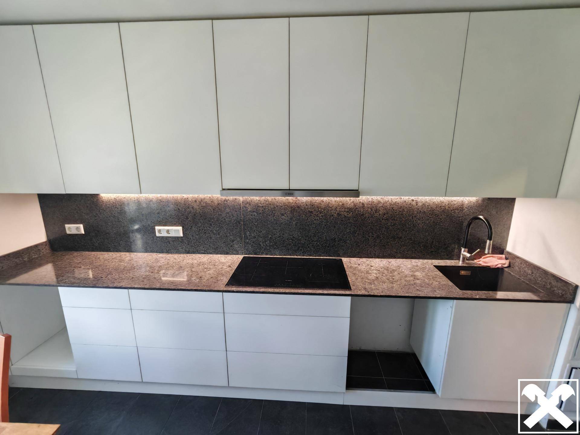 Küchenarbeitsplatte aus Granit mit Induktionskochfeld und Spüle, umgeben von weißen Schränken.