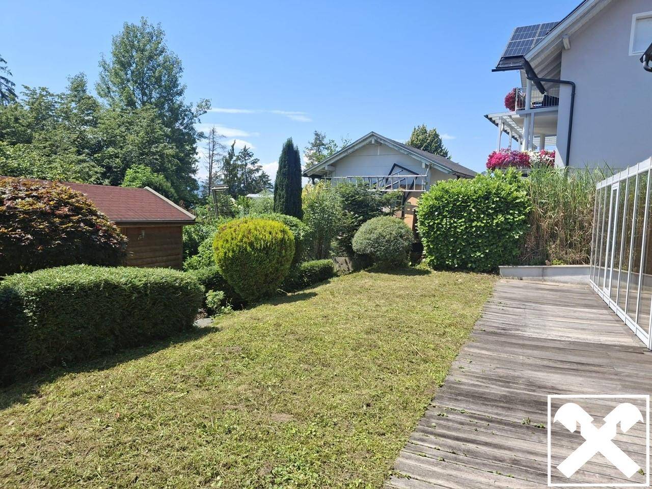 Gepflegter Gartenbereich mit Rasenfläche und Holzterrasse neben dem Haus an einem sonnigen Tag.