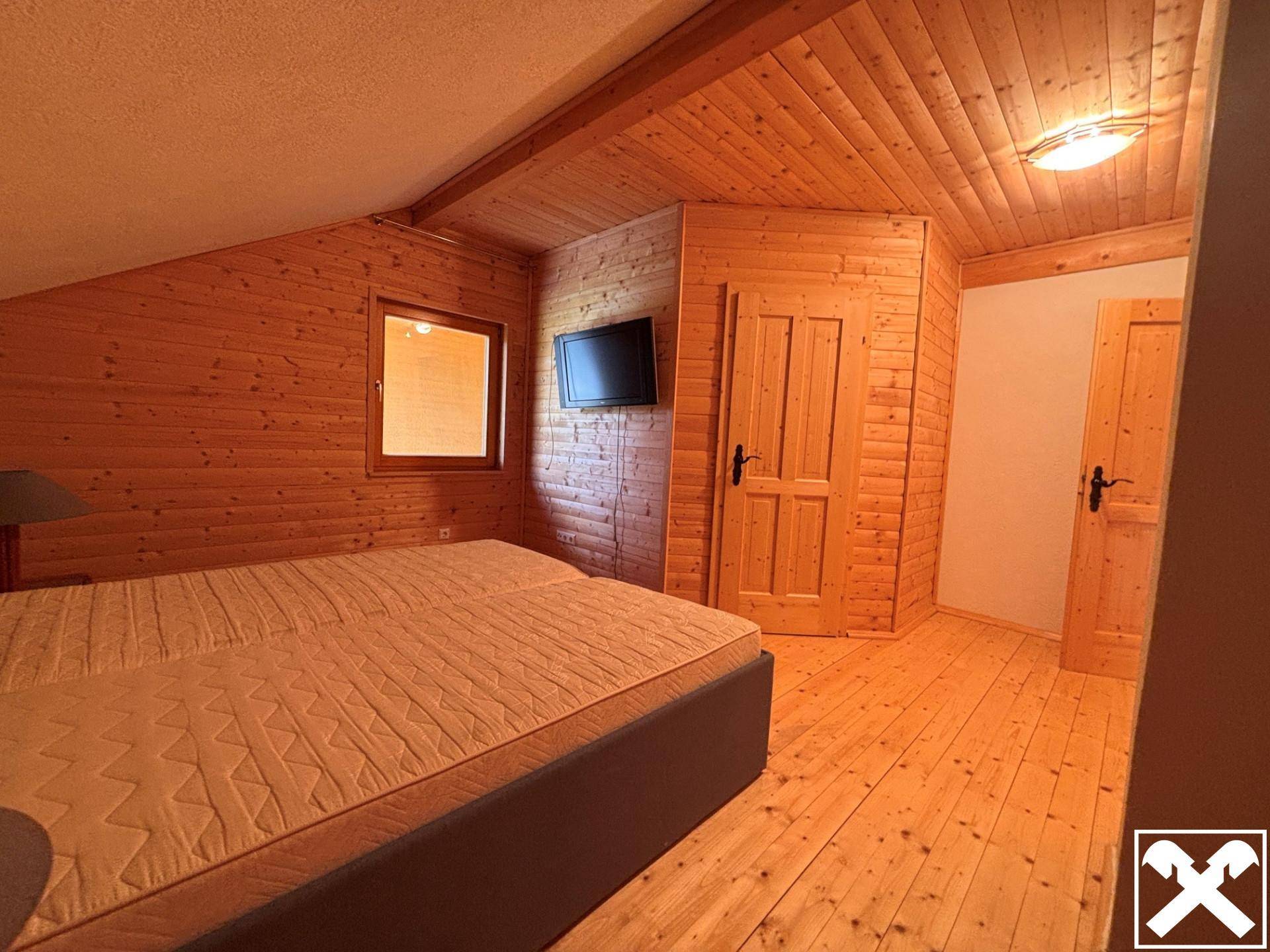 Gemütliches Schlafzimmer mit Holzboden, Holzvertäfelung und einem Doppelbett unter der Dachschräge.