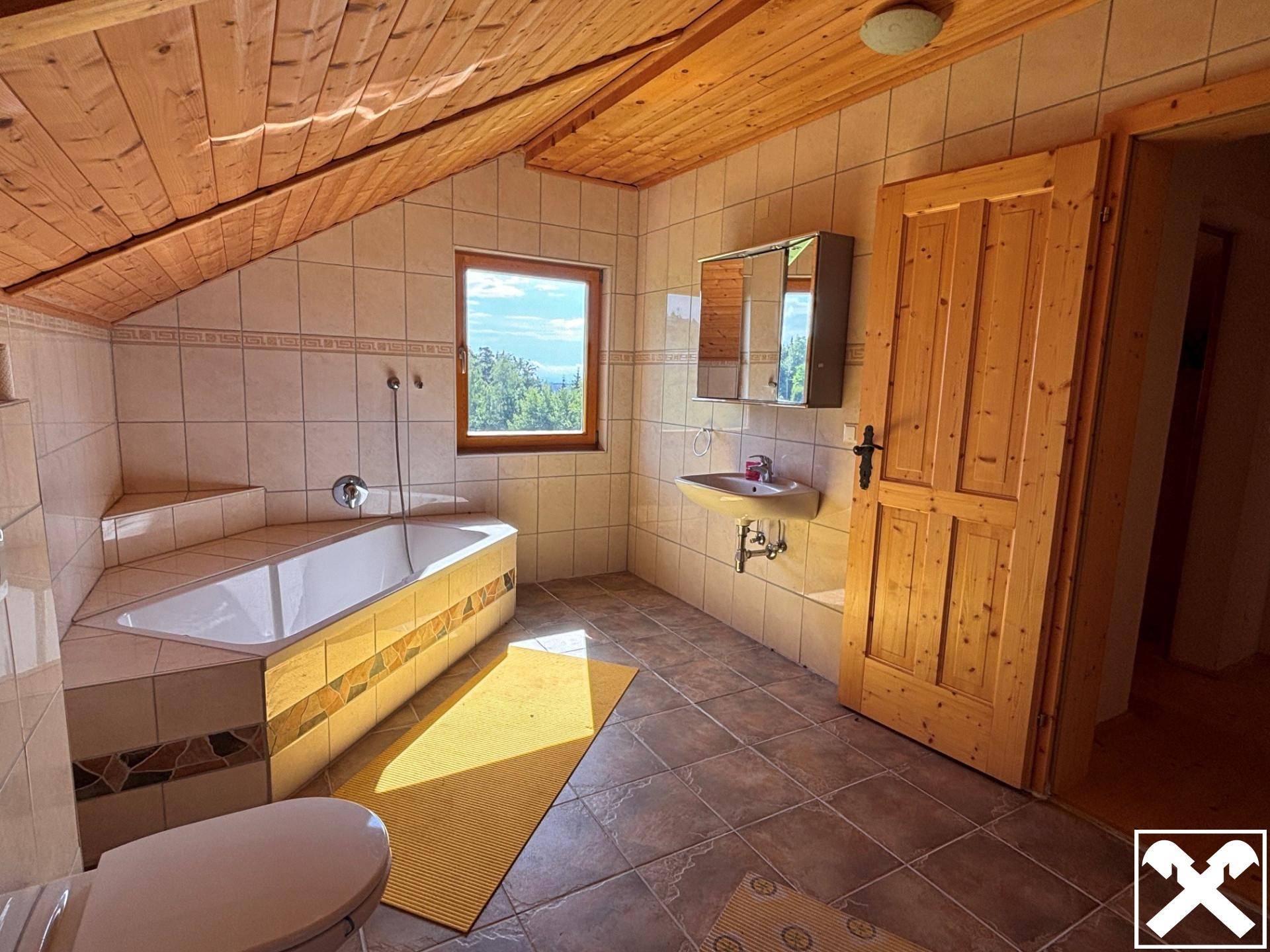 Badezimmer mit Fliesenboden, Holzdecke, Badewanne und Fenster mit Blick ins Grüne.
