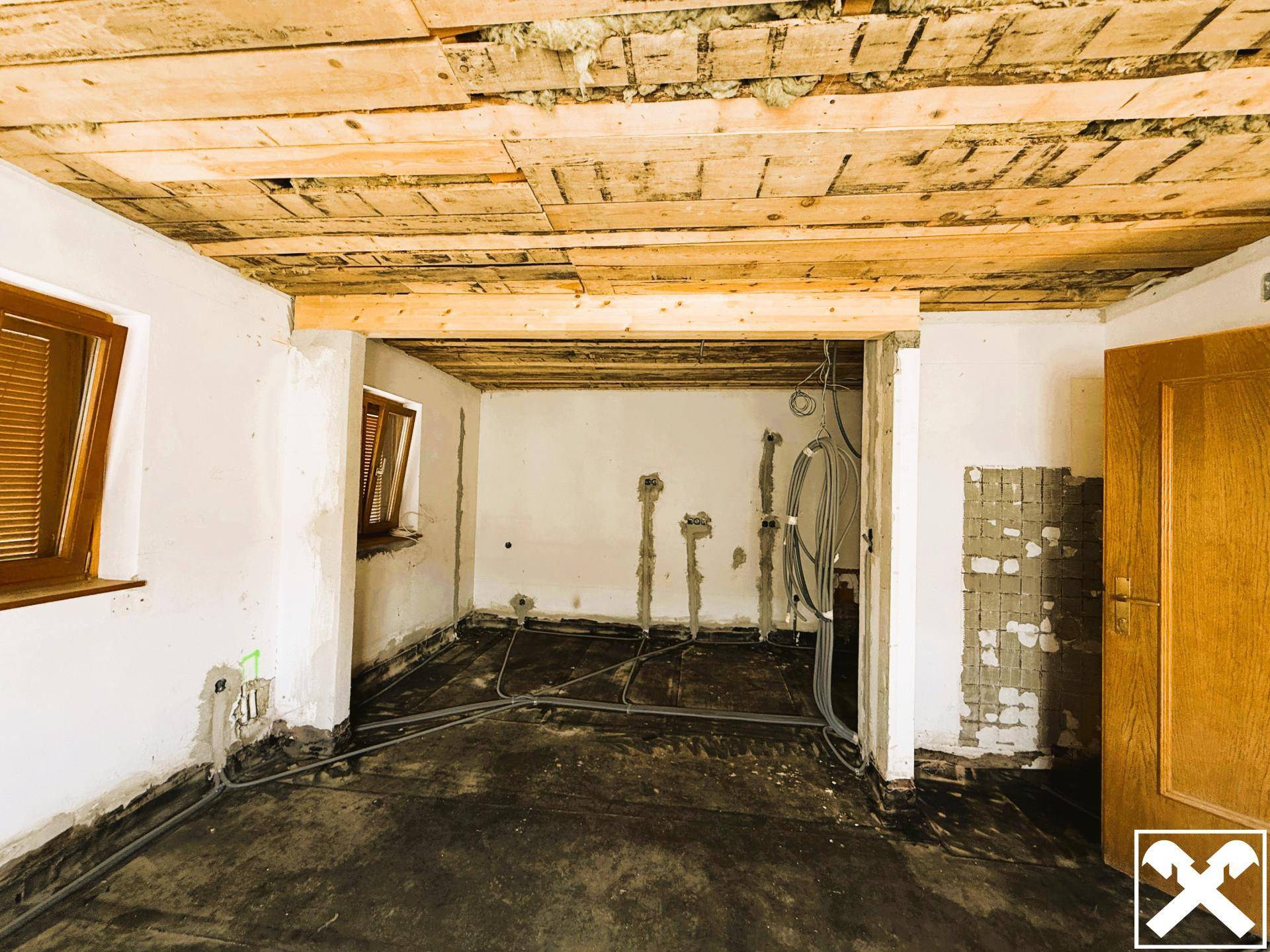 Unfertiger Raum mit freiliegender Holzdecke und vorbereiteten Installationen für die Renovierung.