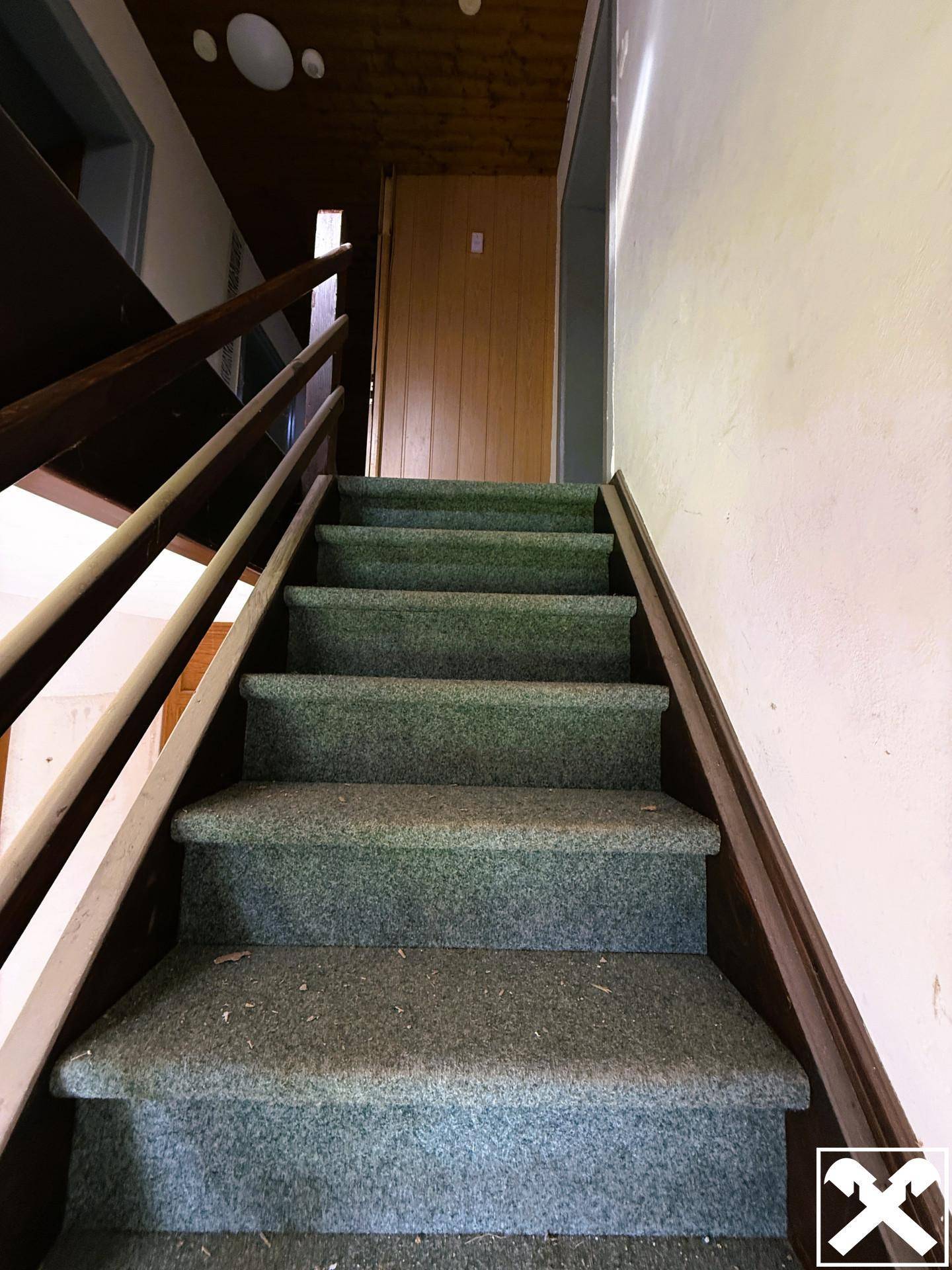 Treppenhaus mit Teppichboden und Holzgeländer, das in die obere Etage führt.