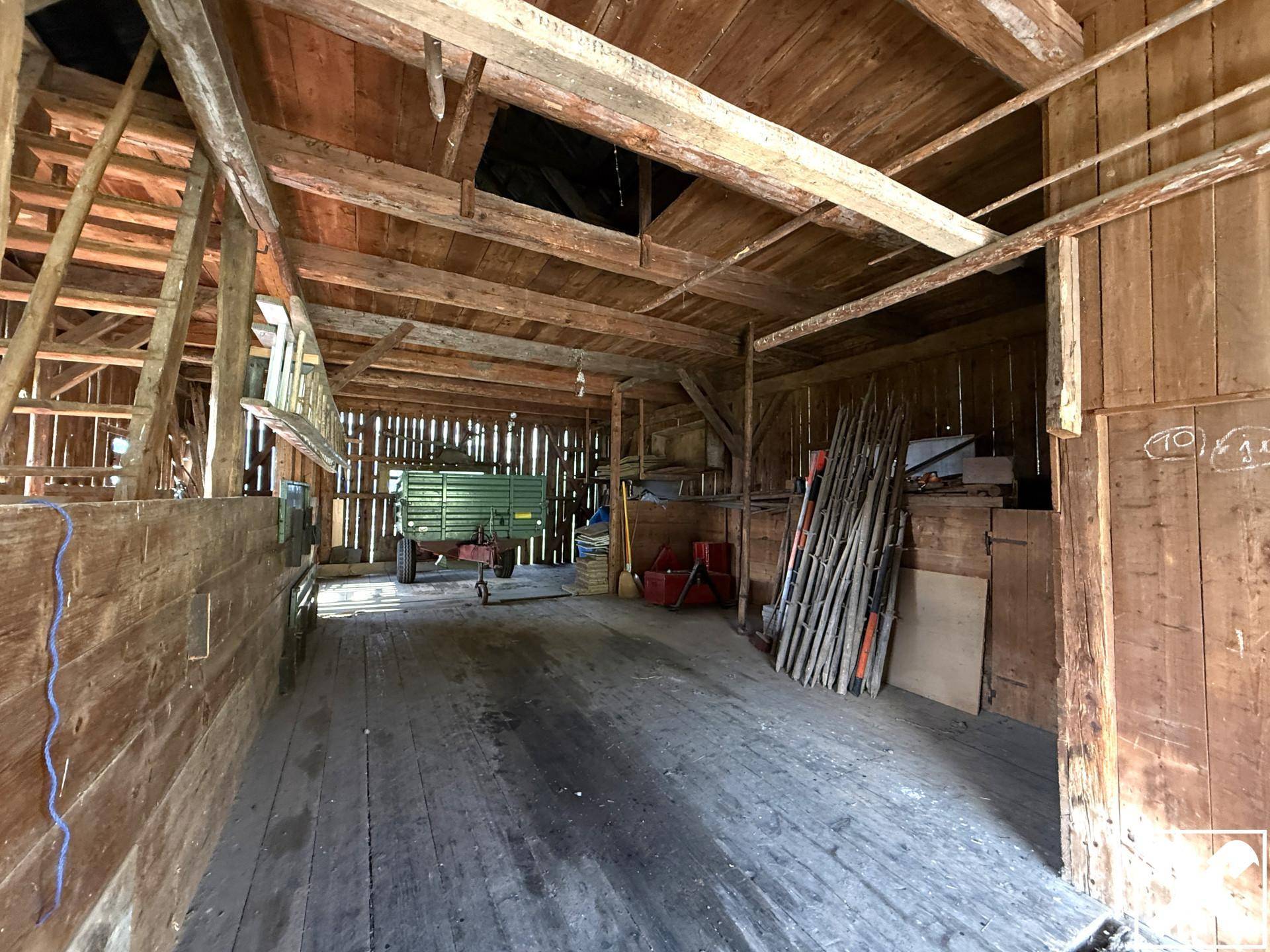 Geräumiger Scheunenbereich mit Holzbalken und Lagerfläche für landwirtschaftliche Geräte.