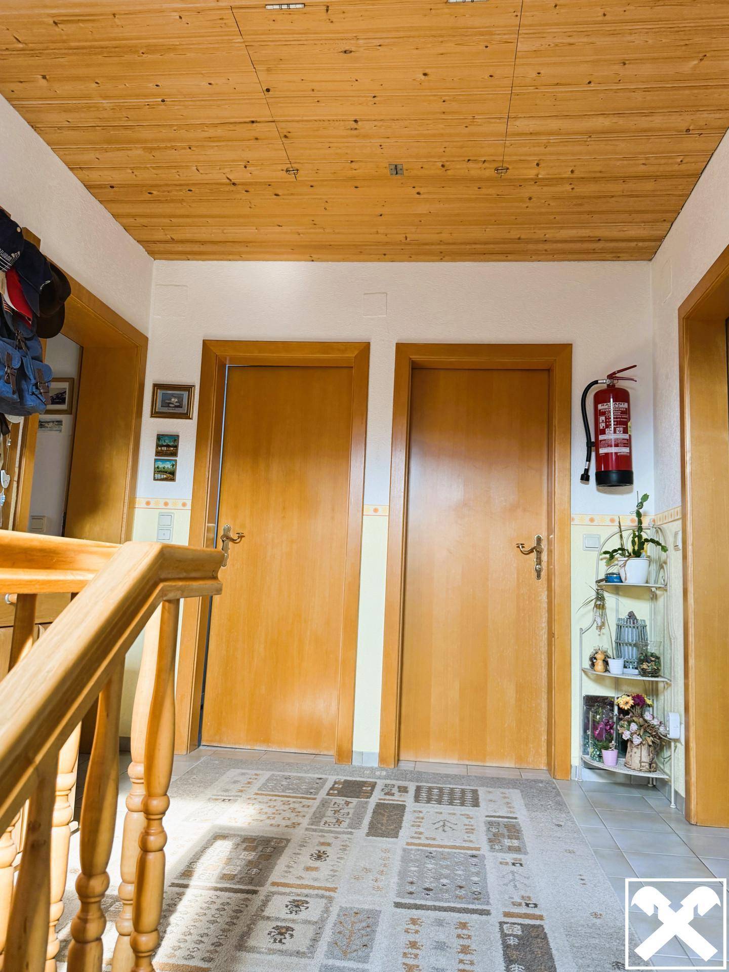 Flur mit Holzdecke und gefliestem Boden, ausgestattet mit mehreren Türen und einem Feuerlöscher an der Wand.