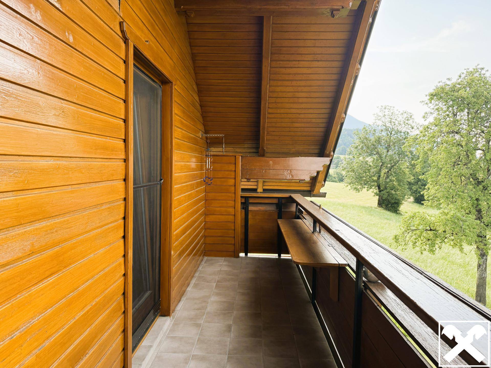 Überdachter Holzbalkon mit Fliesenboden und Sitzbank, bietet einen weiten Blick auf die grüne Landschaft.