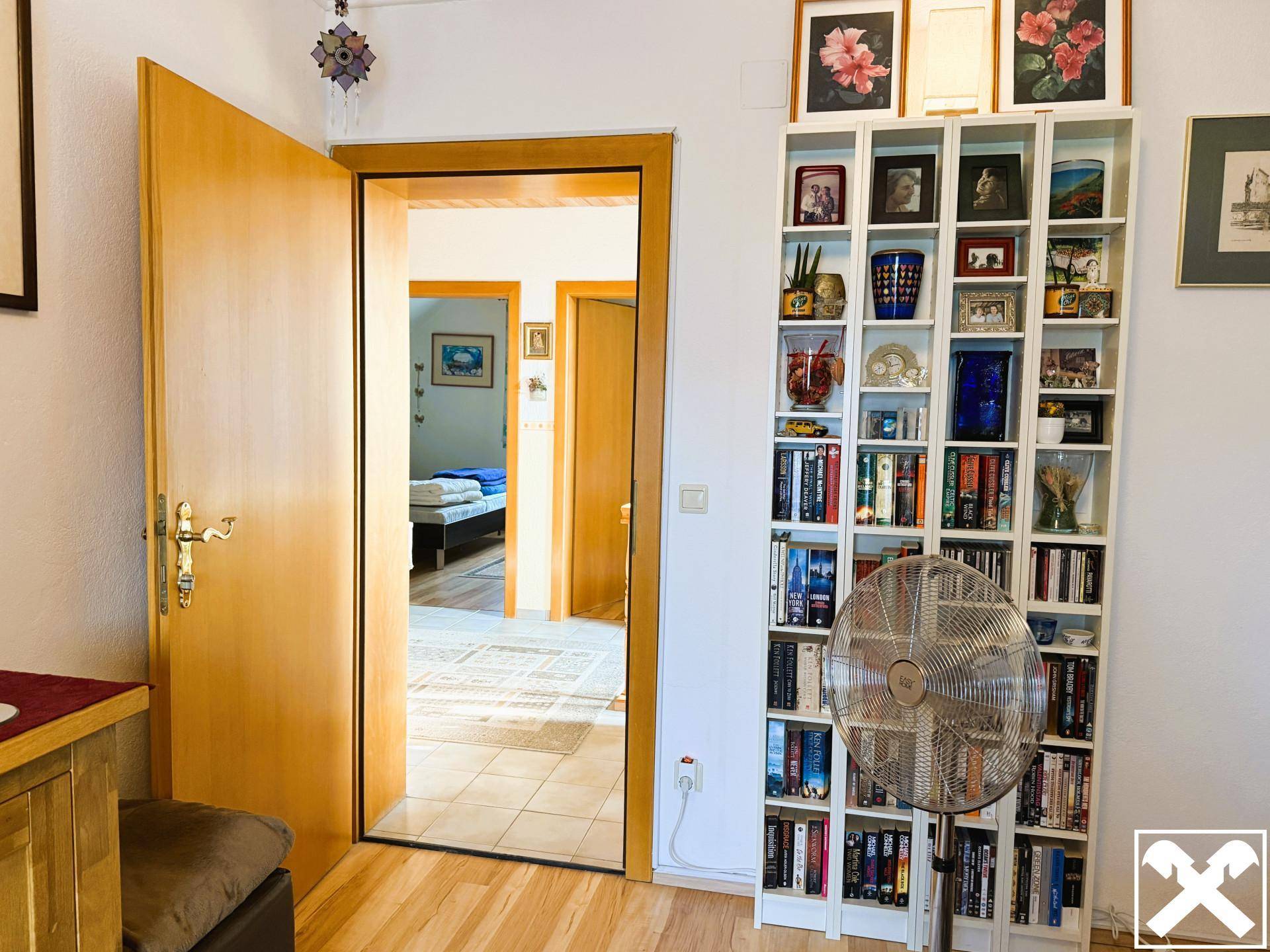 Innenraum mit Bücherregal und offener Tür, die den Blick in ein weiteres Zimmer freigibt.