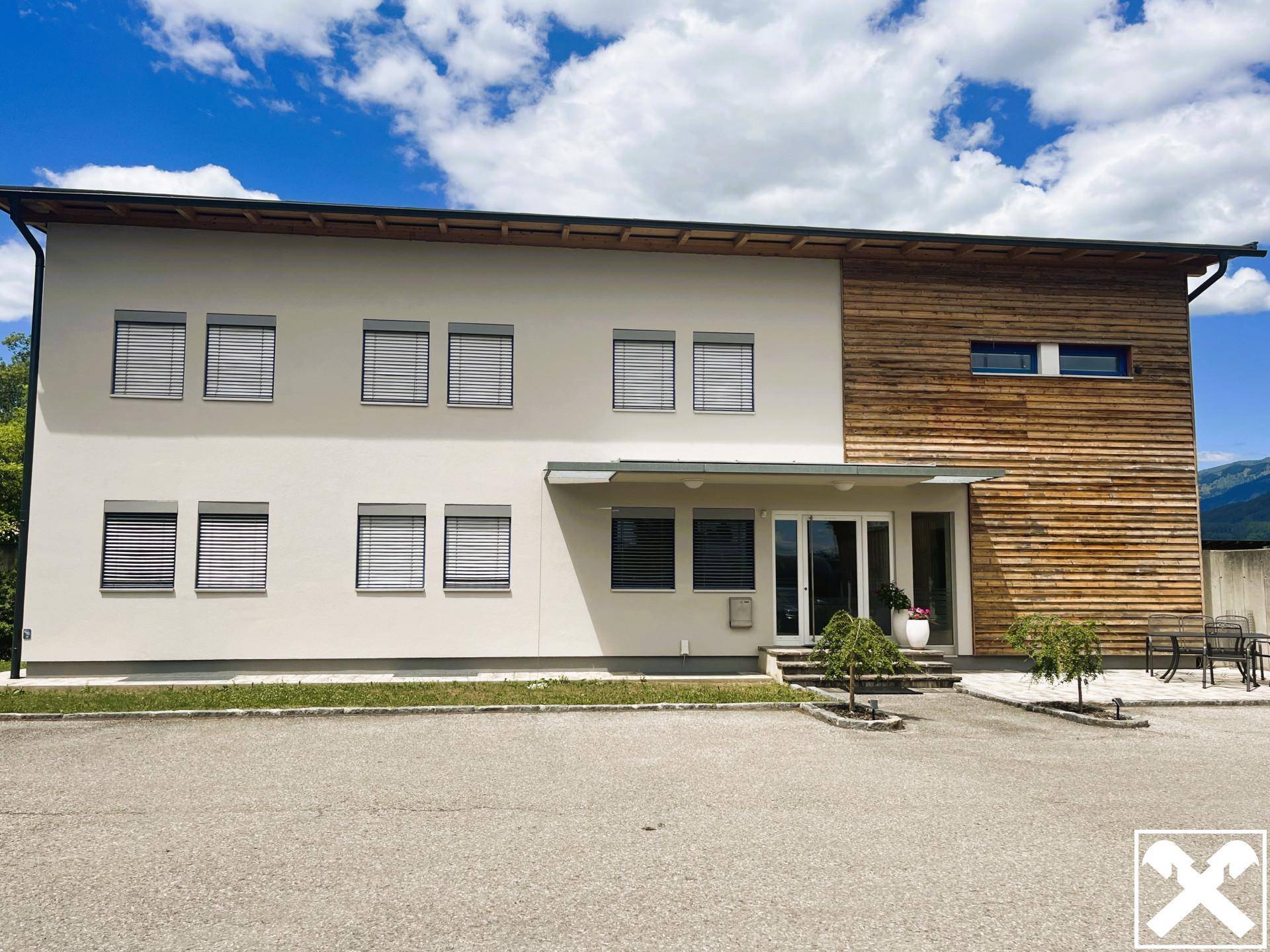 Modernes Geschäftsgebäude mit heller Putzfassade und Holzverkleidung unter blauem Himmel.