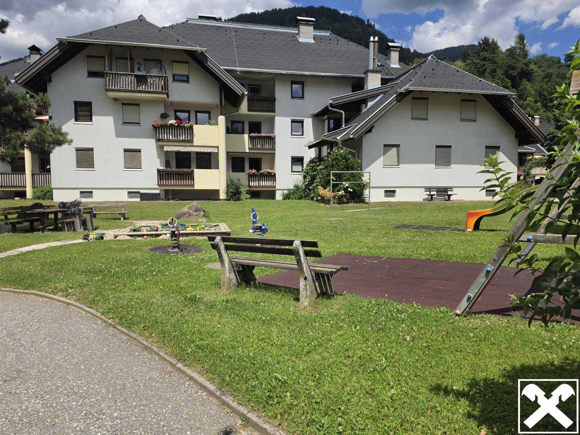 Wohnanlage mit gemeinschaftlichem Gartenbereich, Spielplatz und Blick auf die Berge.