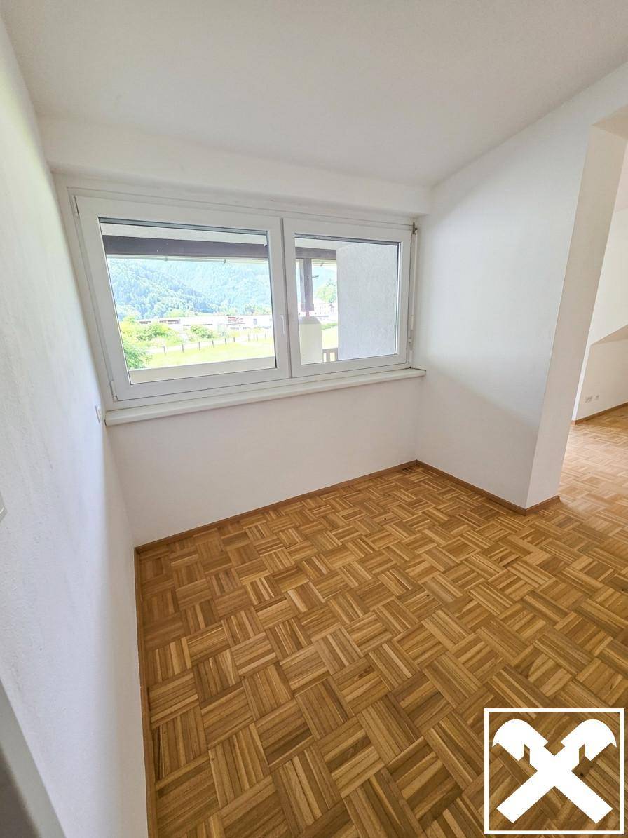Helle Ecke eines Raumes mit Parkettboden und weitem Ausblick auf die grüne Umgebung.