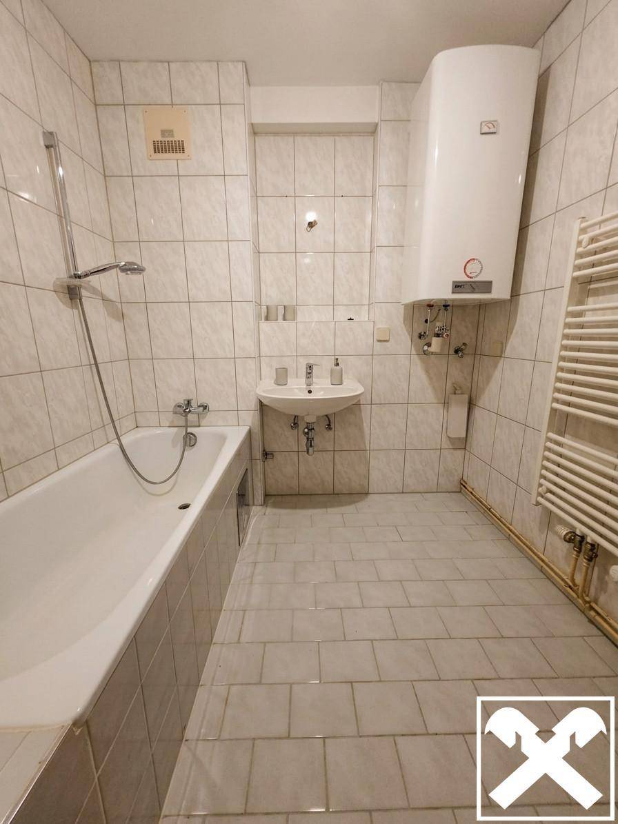 Gefliestes Badezimmer mit Badewanne, kleinem Waschbecken und Wandheizkörper für Handtücher.