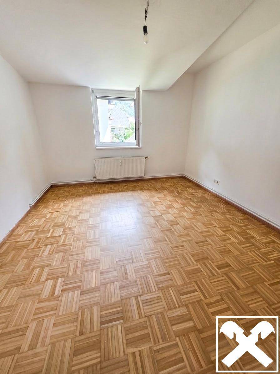 Helles Zimmer mit Parkettboden, weißen Wänden und einem Fenster, ideal als Schlafzimmer.