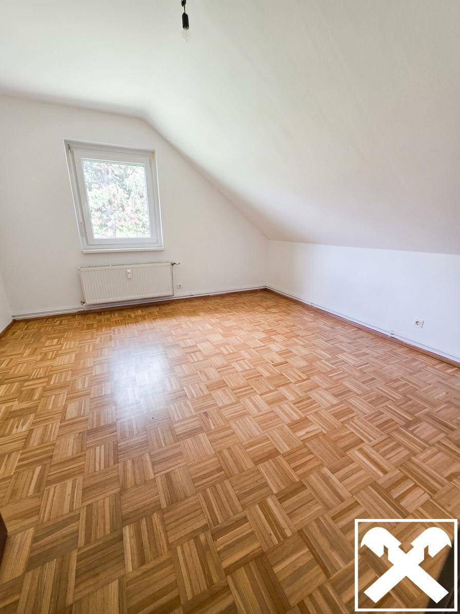 Gemütliches Schlafzimmer mit Parkettboden, Dachschräge und Fenster mit Blick ins Grüne.