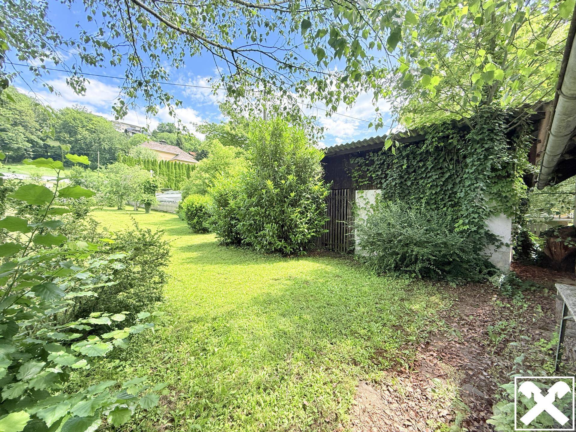 Rustikales Nebengebäude, teilweise mit Efeu bewachsen, inmitten einer grünen Gartenlandschaft.