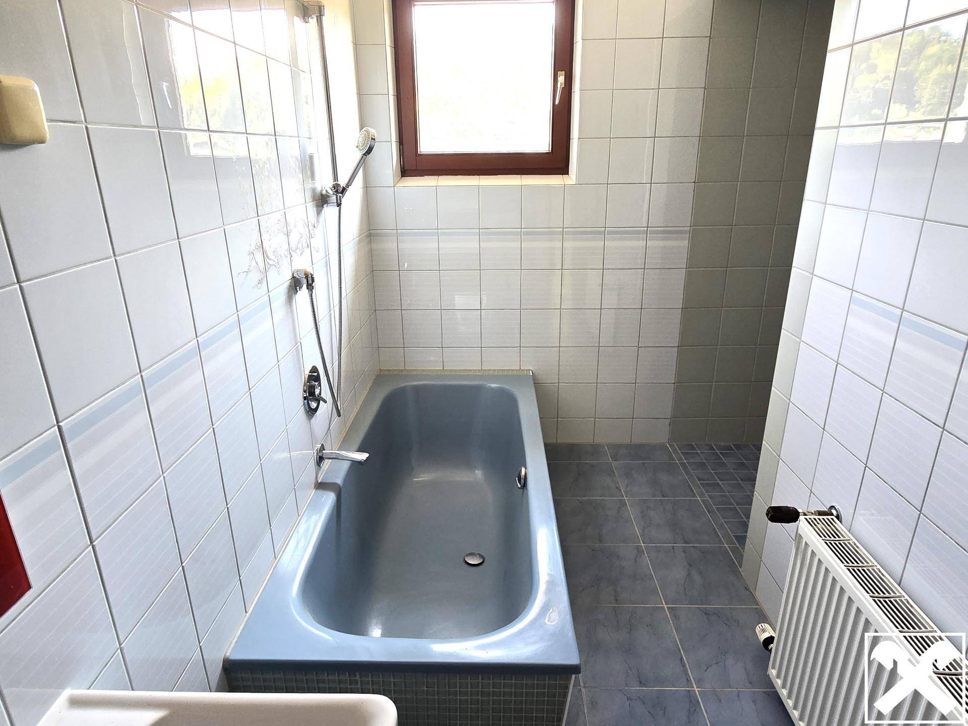 Badezimmer mit blauen Fliesen, Badewanne und Duschbereich sowie einem Fenster.