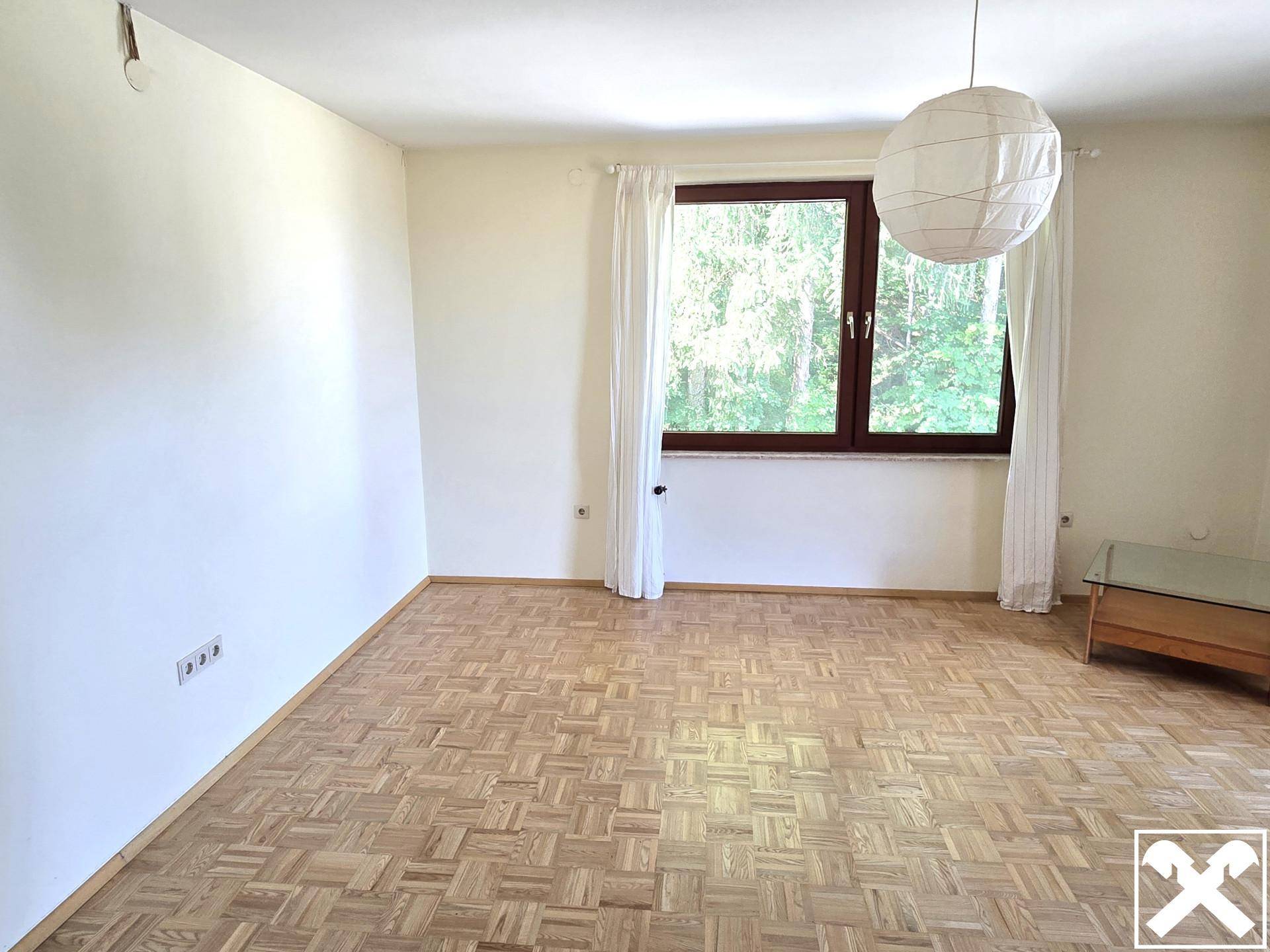 Helles Zimmer mit Parkettboden und einem Fenster mit Blick auf die Bäume.