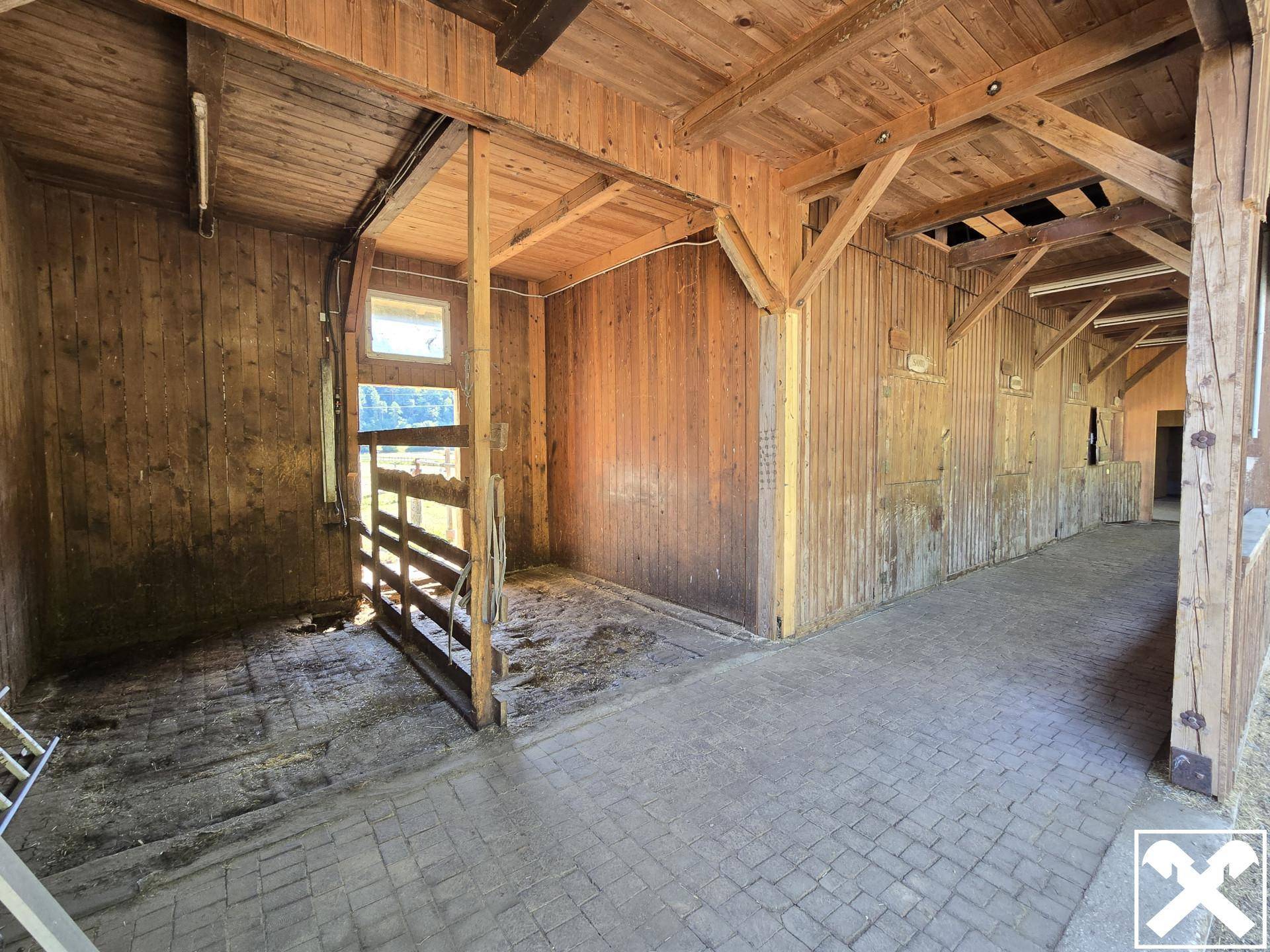 Innenbereich einer Holzscheune mit Stallboxen und gepflastertem Boden.