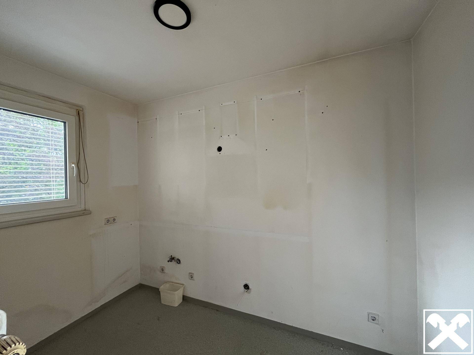 Leerer Küchenraum mit Anschlüssen für Geräte und Fenster für natürliche Belüftung, bereit zur Gestaltung.