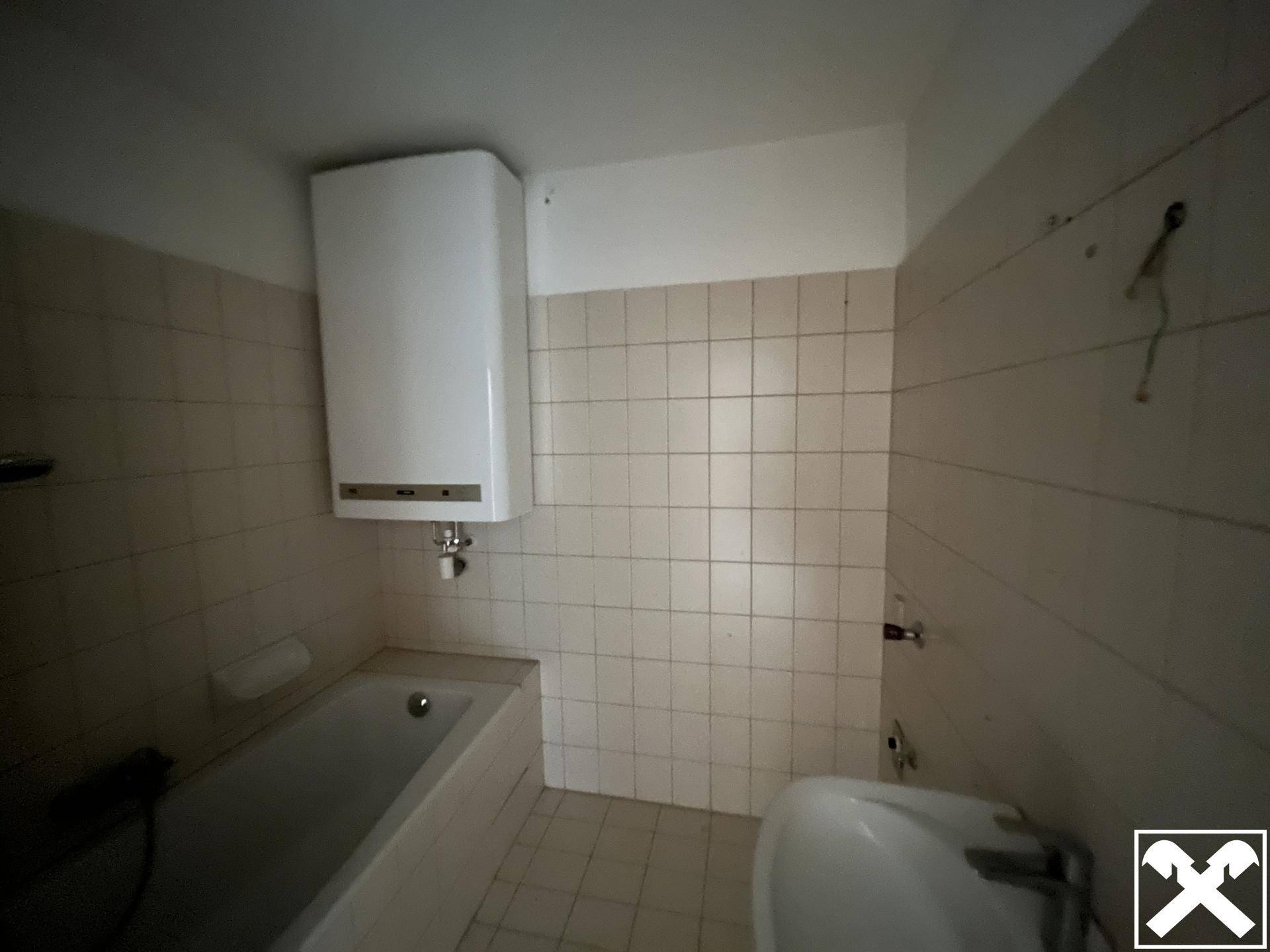 Badezimmer mit Badewanne, Waschbecken und hellen Fliesen, bereit zur Renovierung und Modernisierung.