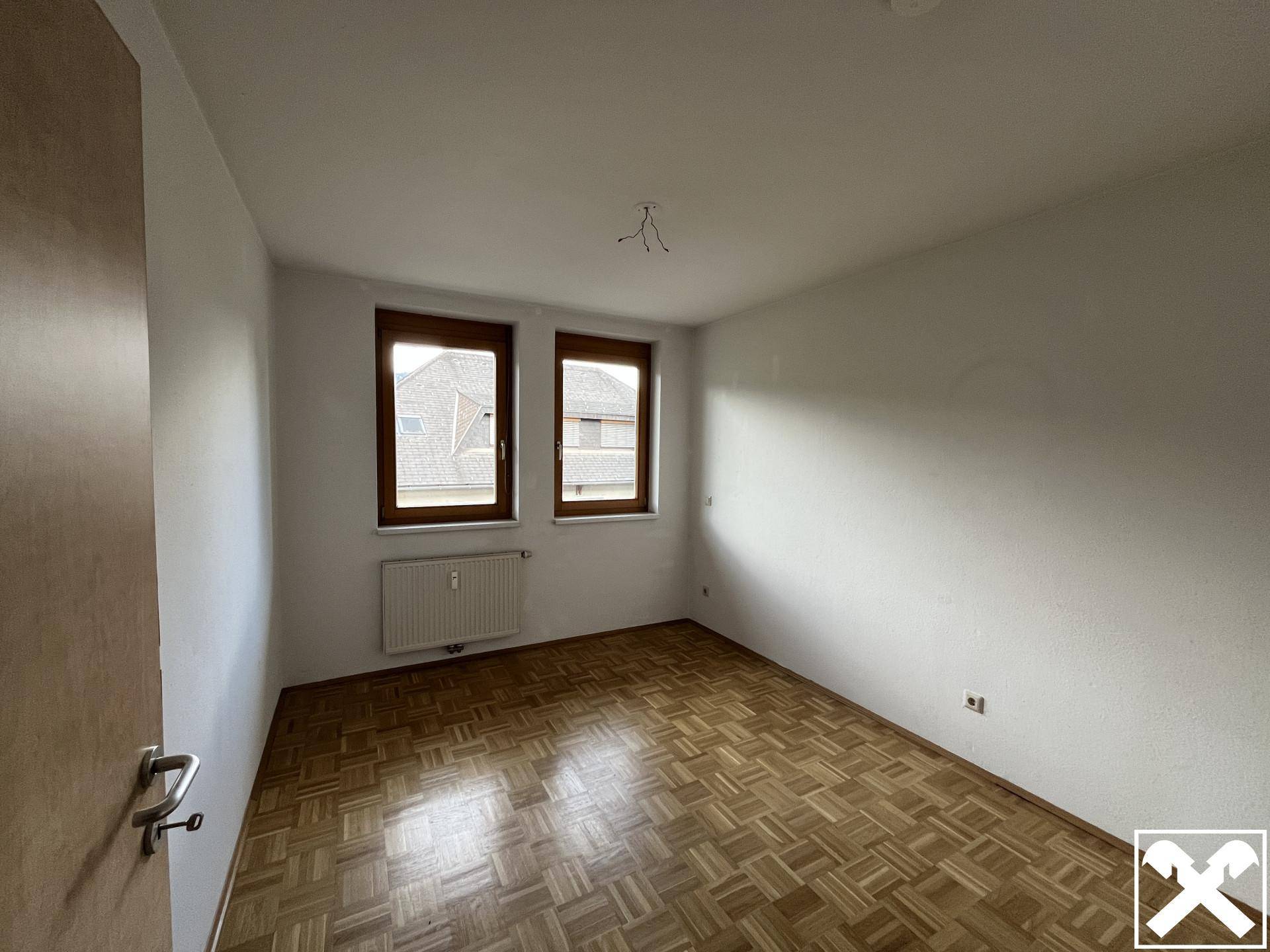 Schlafzimmer mit Parkettboden, zwei Fenstern und ausreichend Tageslicht.