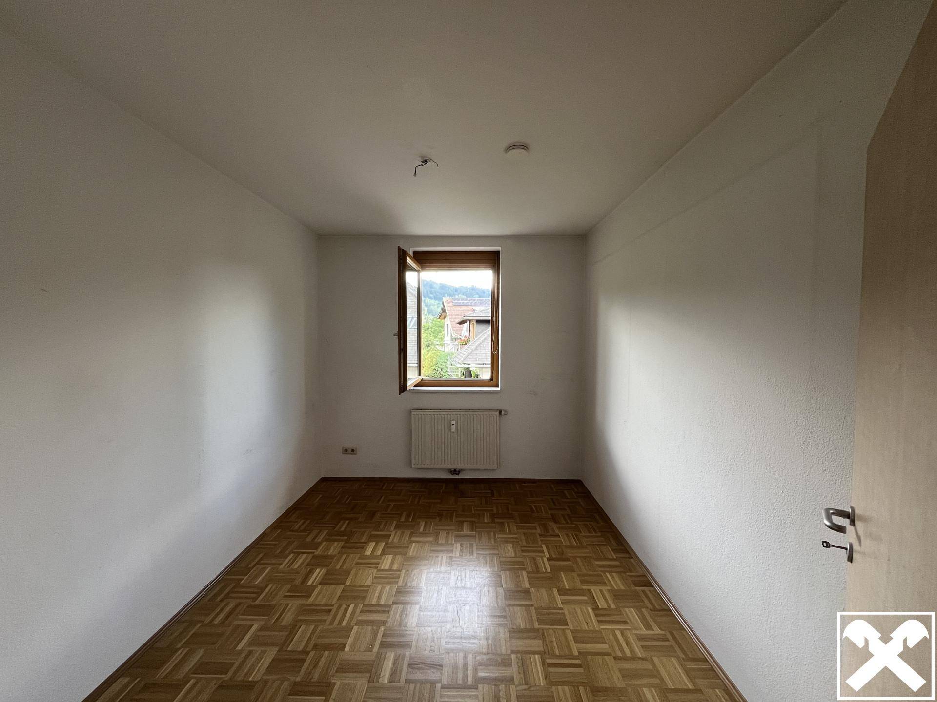 Weiteres Schlafzimmer mit Parkettboden und einem Fenster mit Blick ins Grüne.