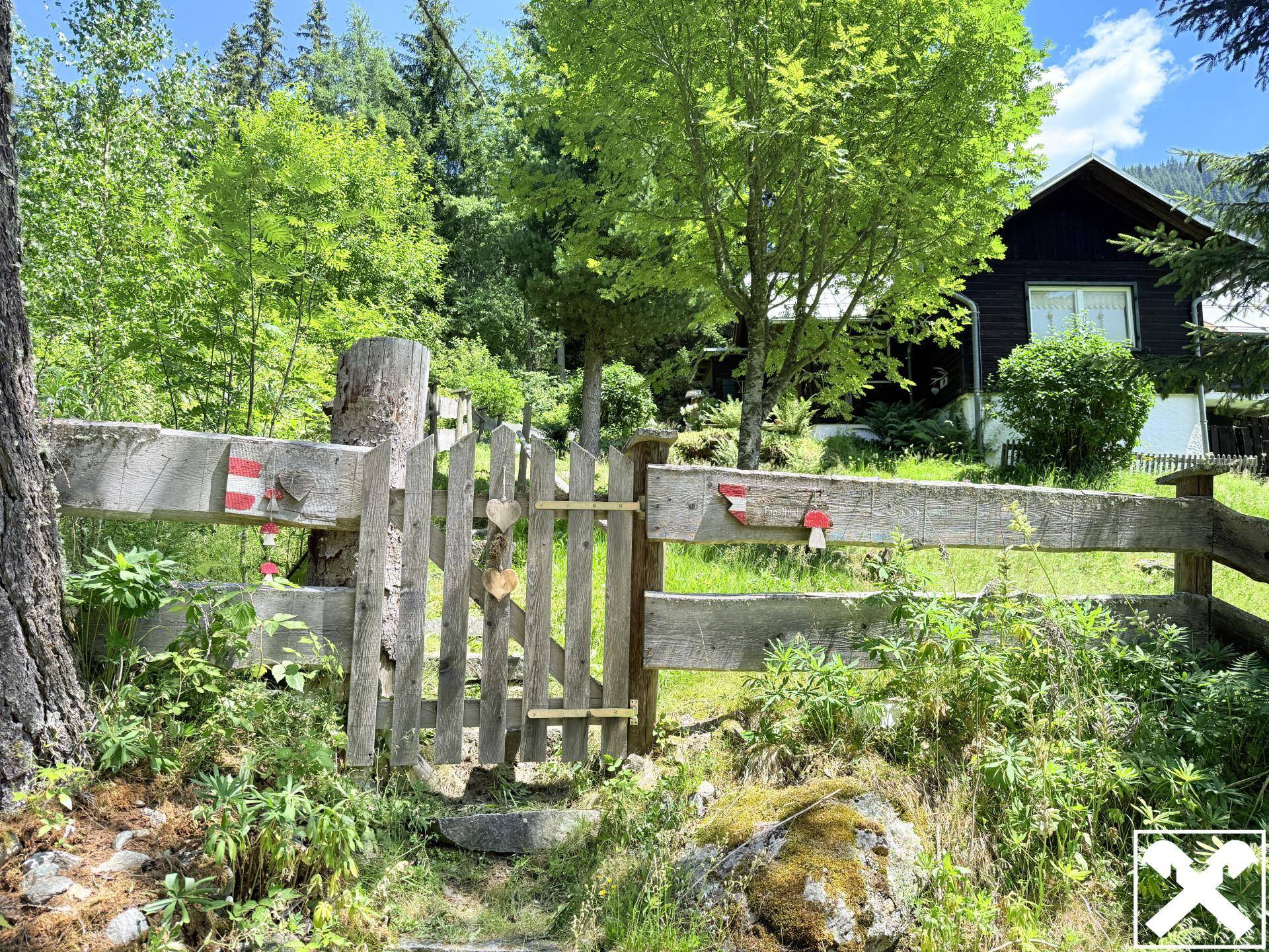 Rustikaler Holzzaun mit Tor, der den Eingang zum Anwesen in der grünen Landschaft markiert.