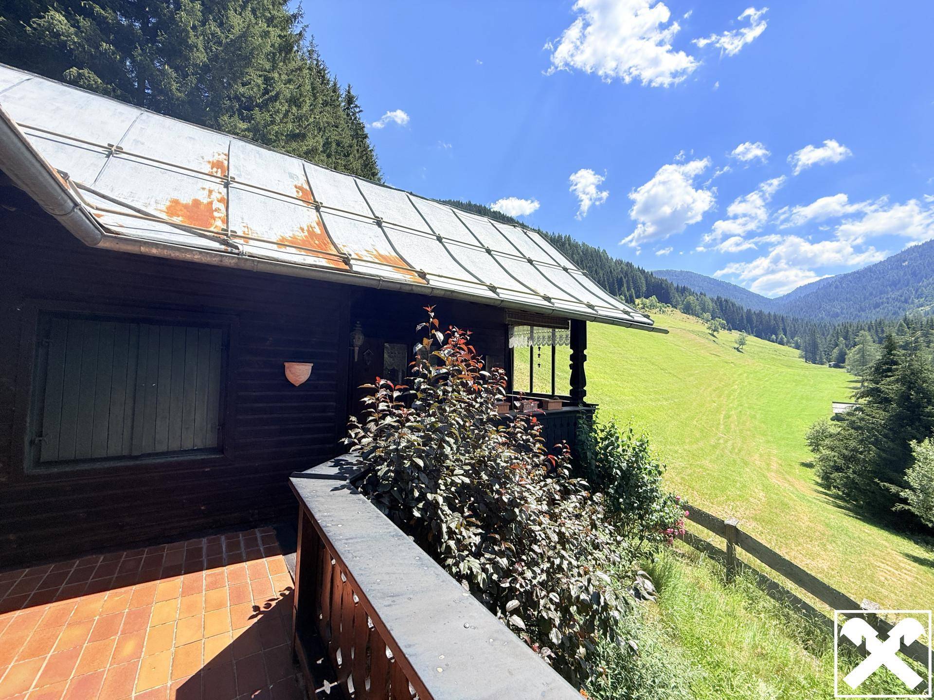 Balkon mit rustikalen Fliesen und weitem Blick über grüne Wiesen und bewaldete Berge.