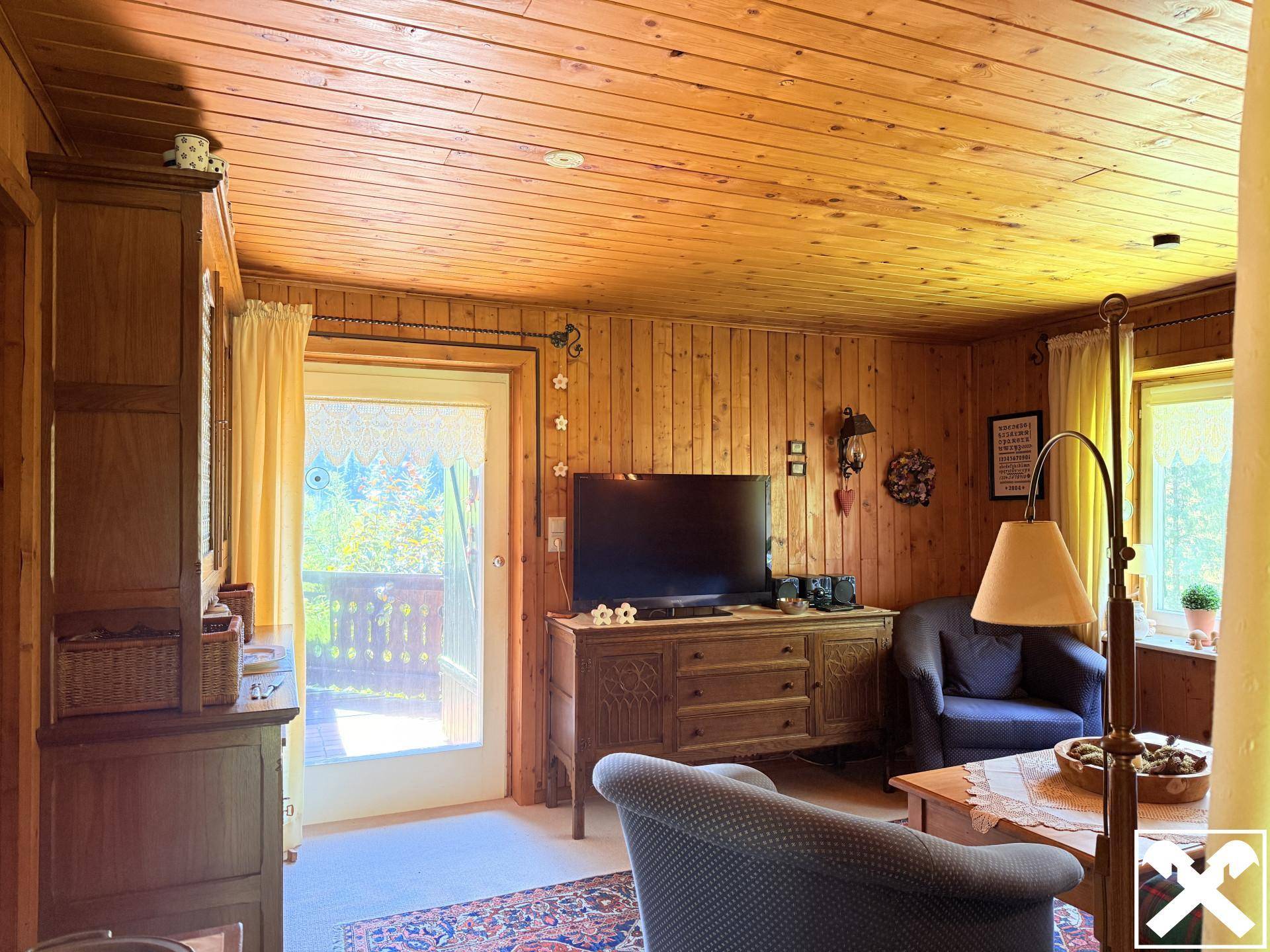 Gemütliches Wohnzimmer im alpinen Stil mit Holzvertäfelung, Teppich und Zugang zum Balkon.