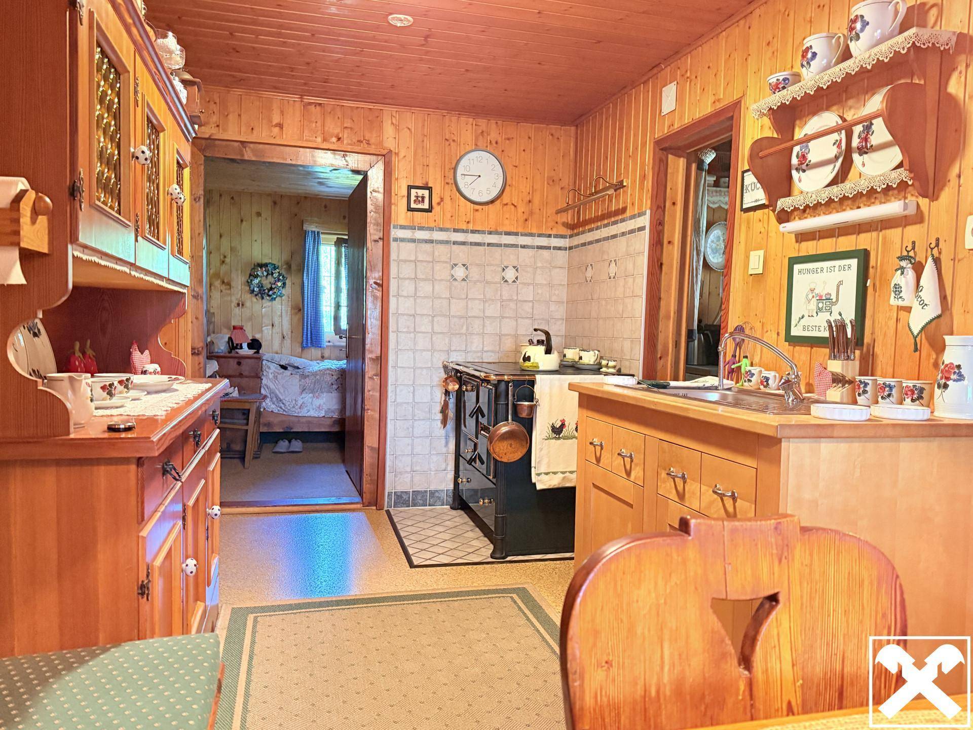 Traditionelle Holzküche mit Kachelofen und Durchgang zu einem weiteren Zimmer im alpinen Stil.