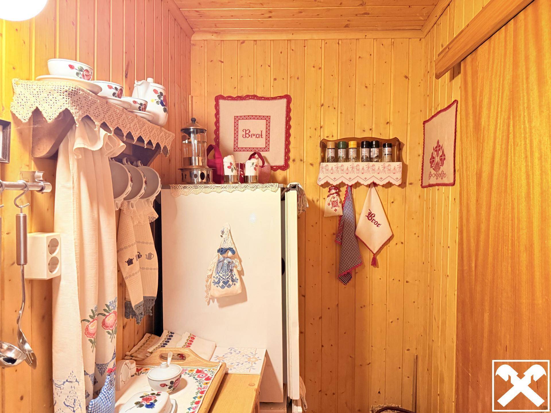 Detailansicht einer traditionellen Küche mit Kühlschrank und rustikalen Dekorationen an der Holzwand.