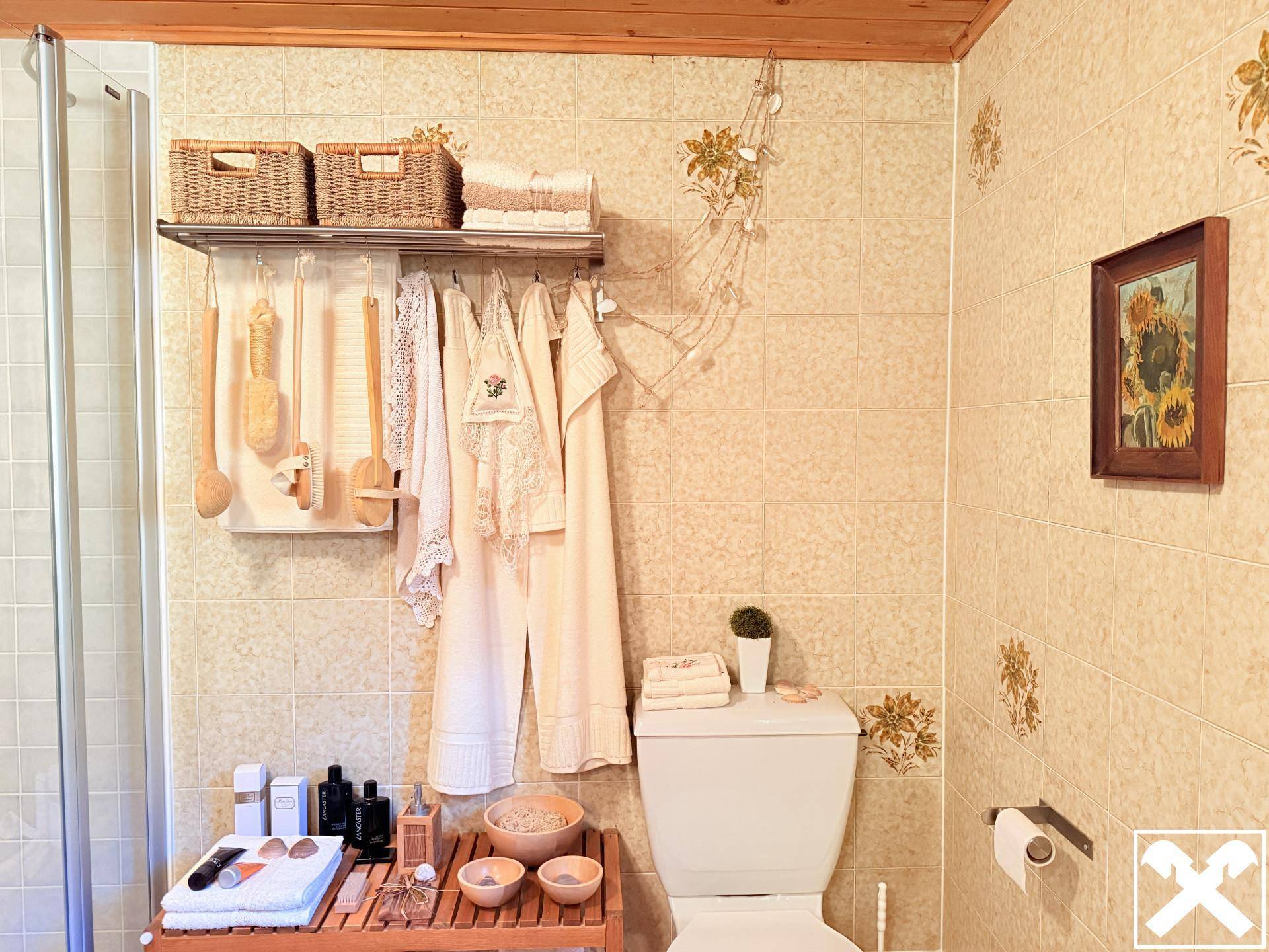 Einfaches WC mit beigefarbenen Fliesen, Duschbereich und rustikalen Holzdetails.