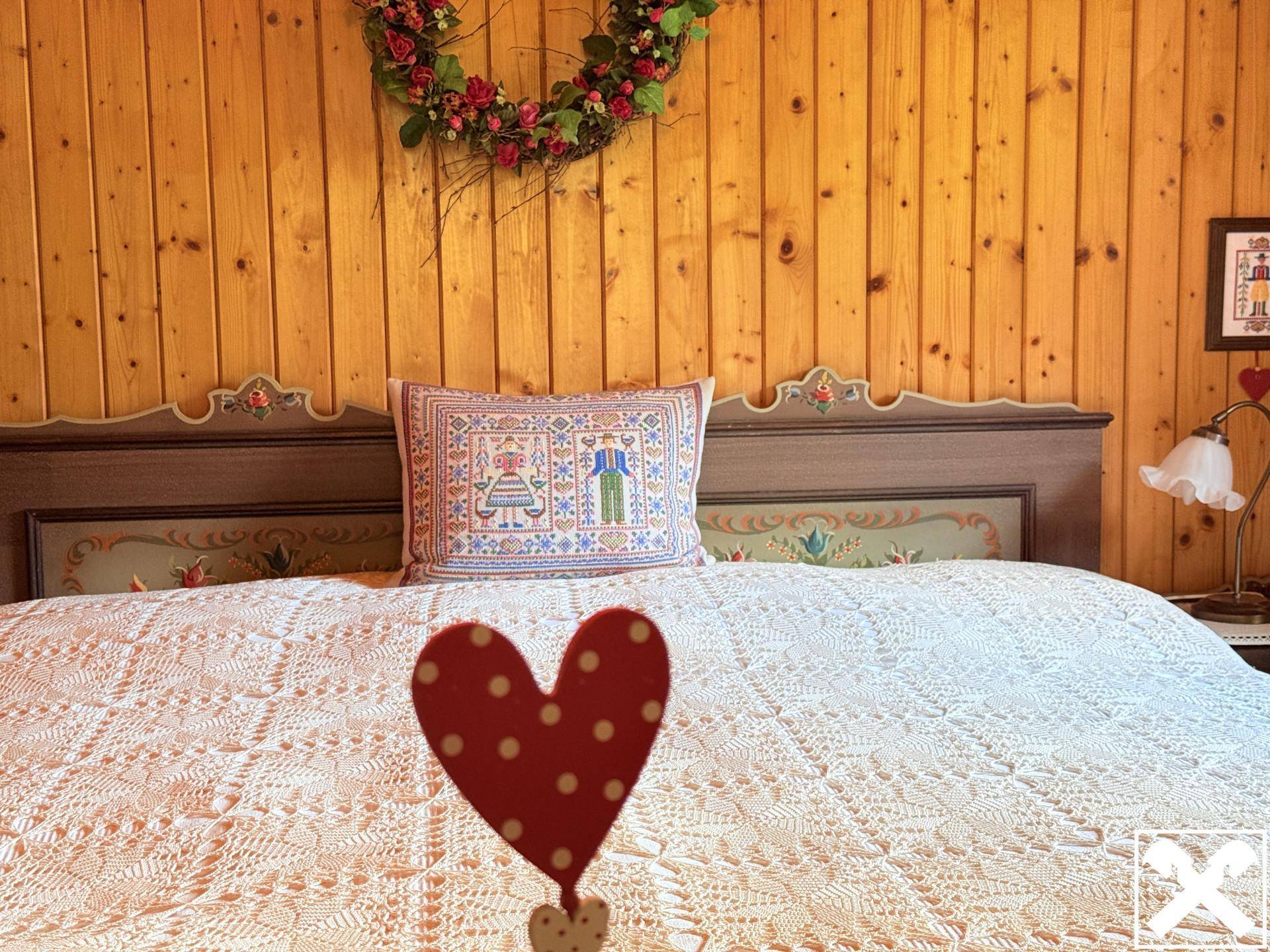 Detailansicht eines Bettes mit traditioneller Bettwäsche und Holzkopfteil im Schlafzimmer.