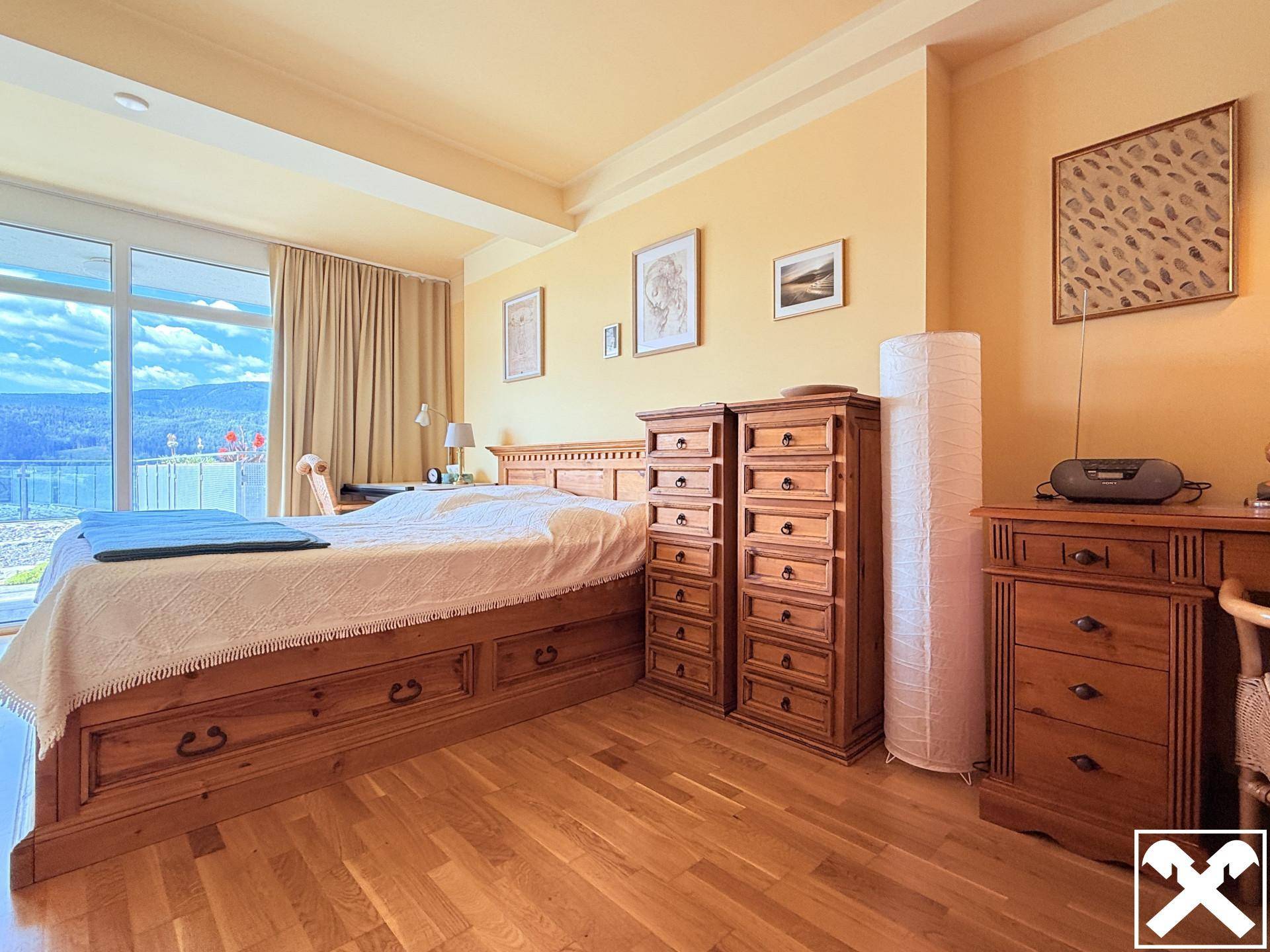 Helles Schlafzimmer mit großem Holzbett, passenden Kommoden und Zugang zu einem Balkon mit schöner Aussicht.