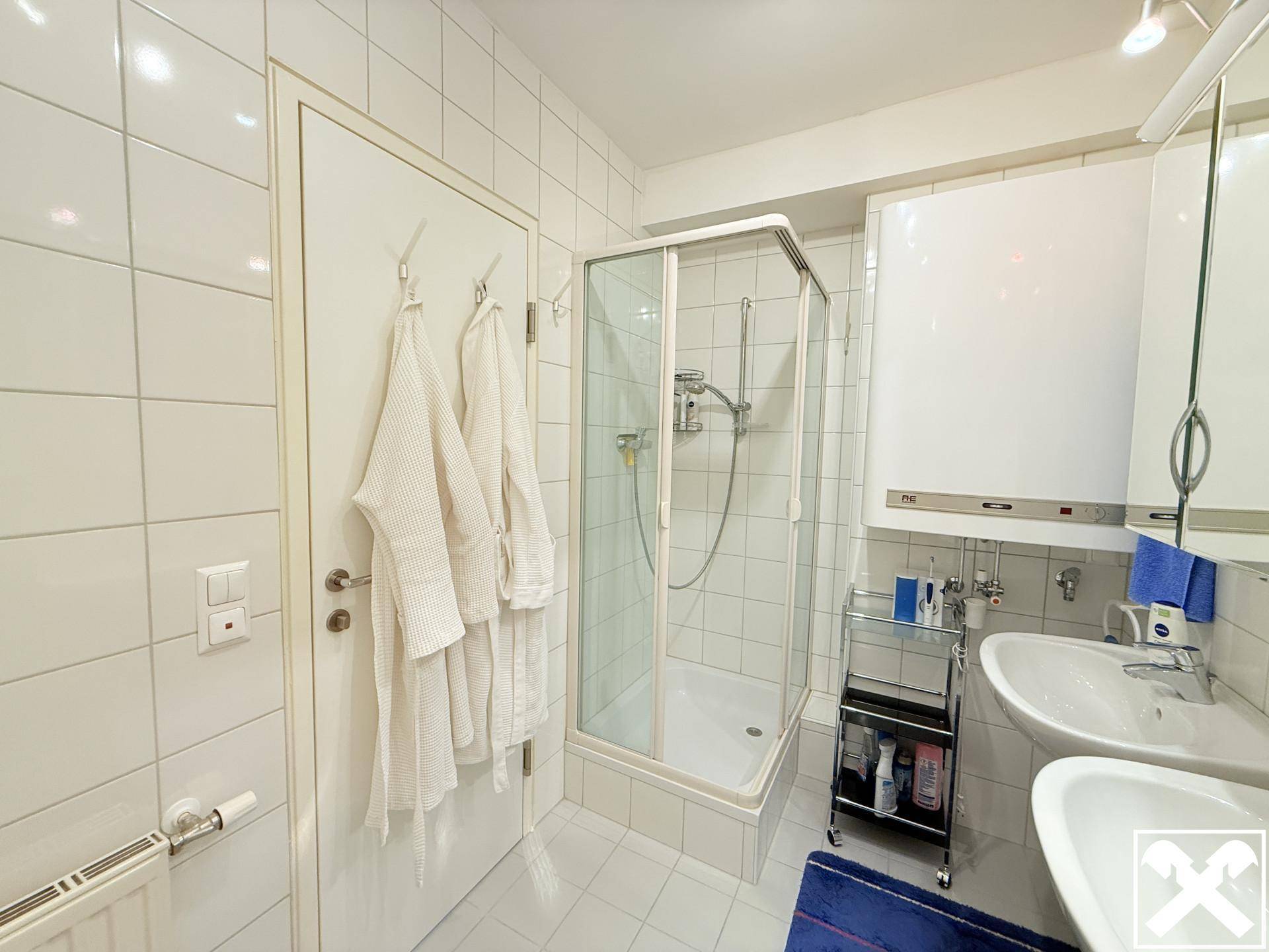 Modernes Badezimmer mit weißen Fliesen, Duschkabine und Waschbecken, ausgestattet mit praktischen Armaturen.